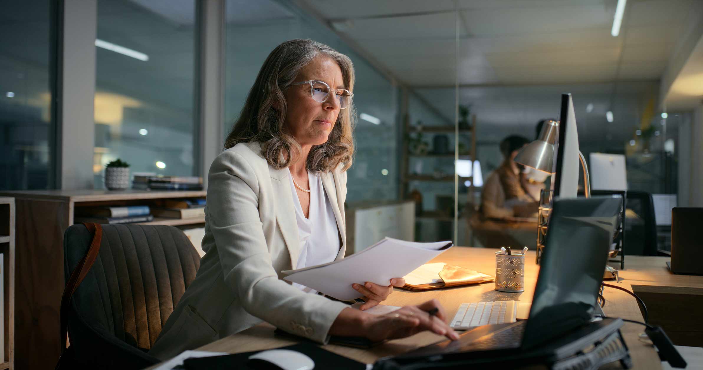 Woman in glasses working on Legal Automation Enablement at her desk in a modern office at night.