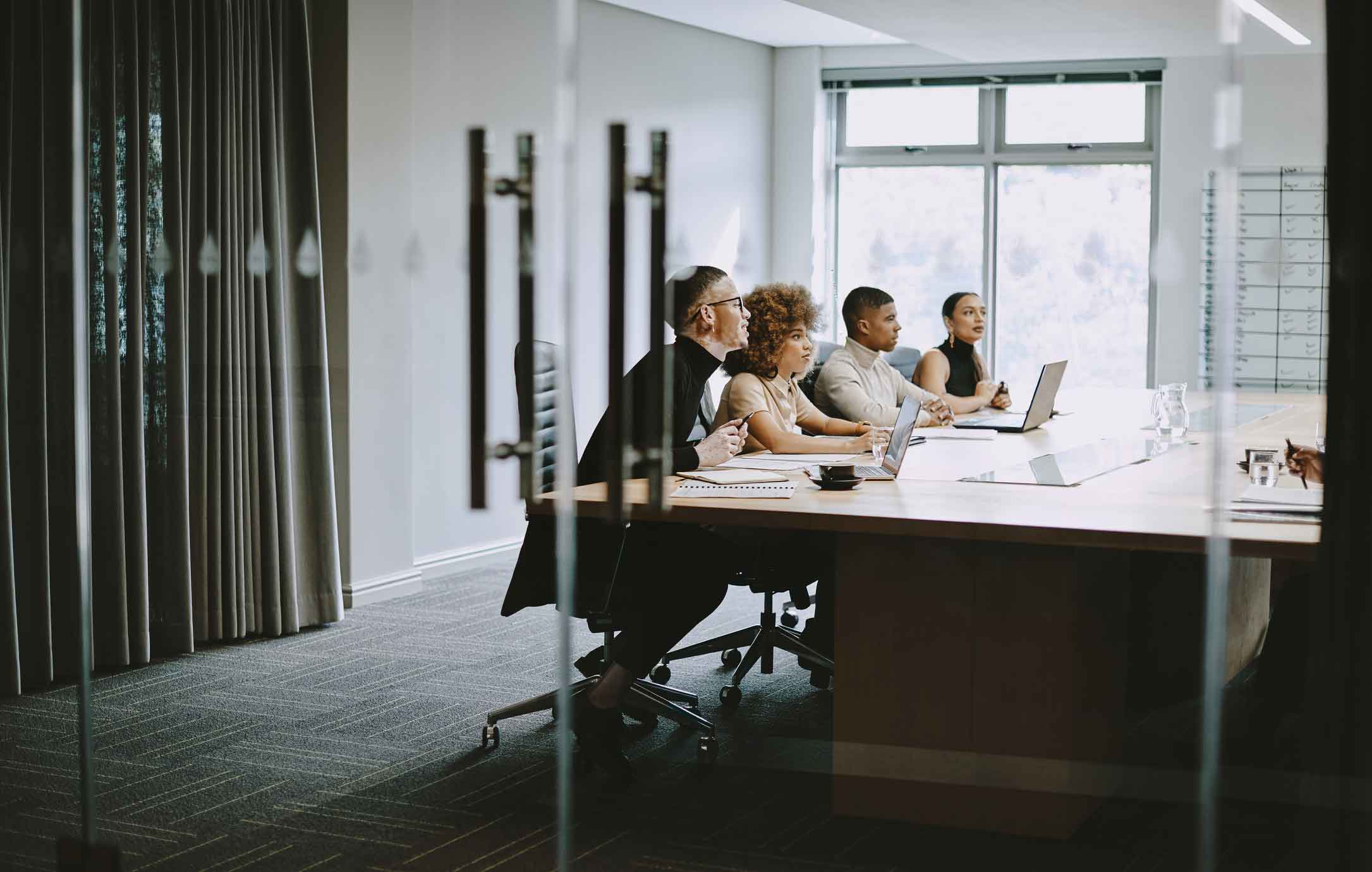Four people discuss cybersecurity compliance at a conference table during a technology meeting.
