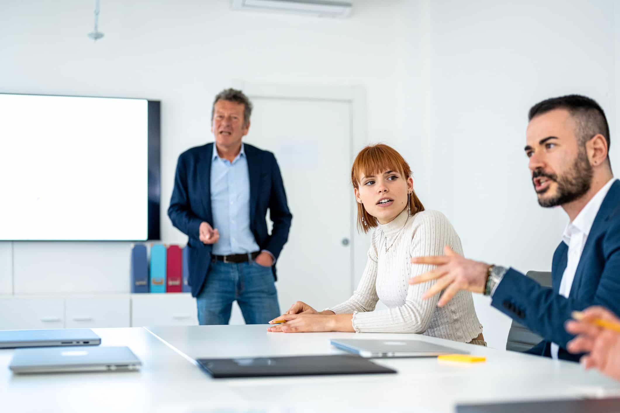 Three people in a meeting room discuss mergers & Acquisition integration consulting strategies.