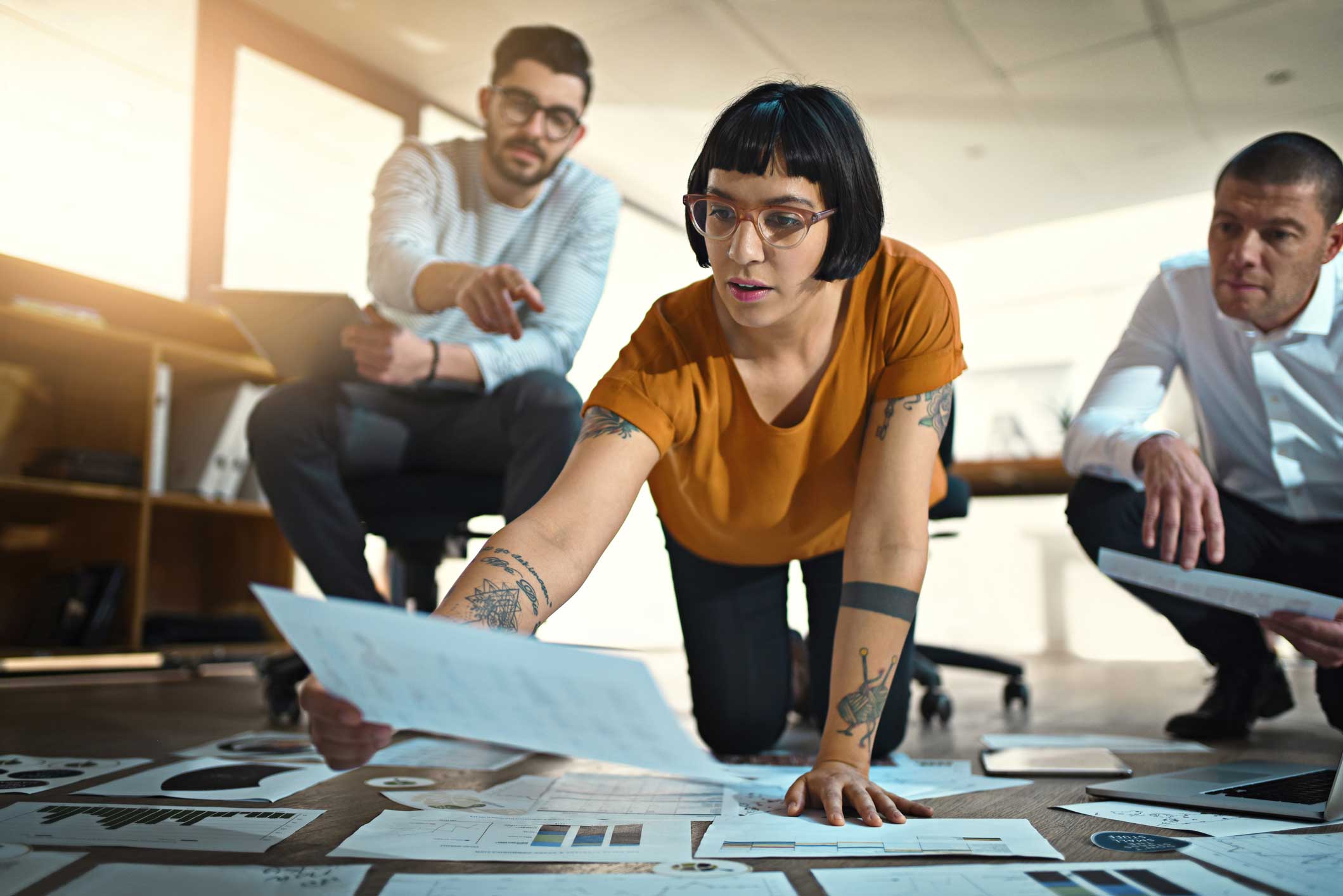 Three people conducting Digital Forensics Advisory, analyzing documents on a bright office floor.