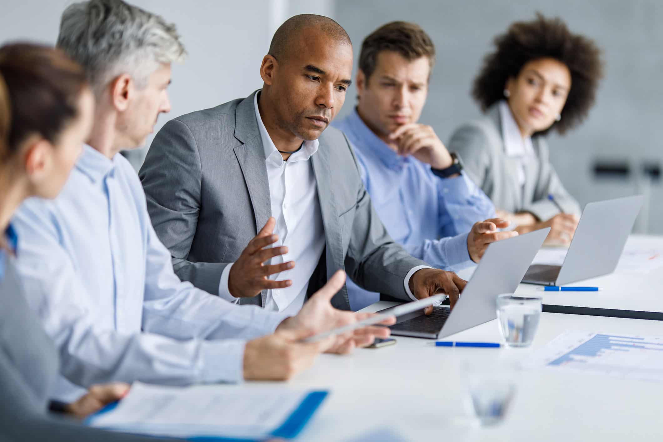Five people discuss Forensic Litigation Consulting around a conference table with laptops & papers.