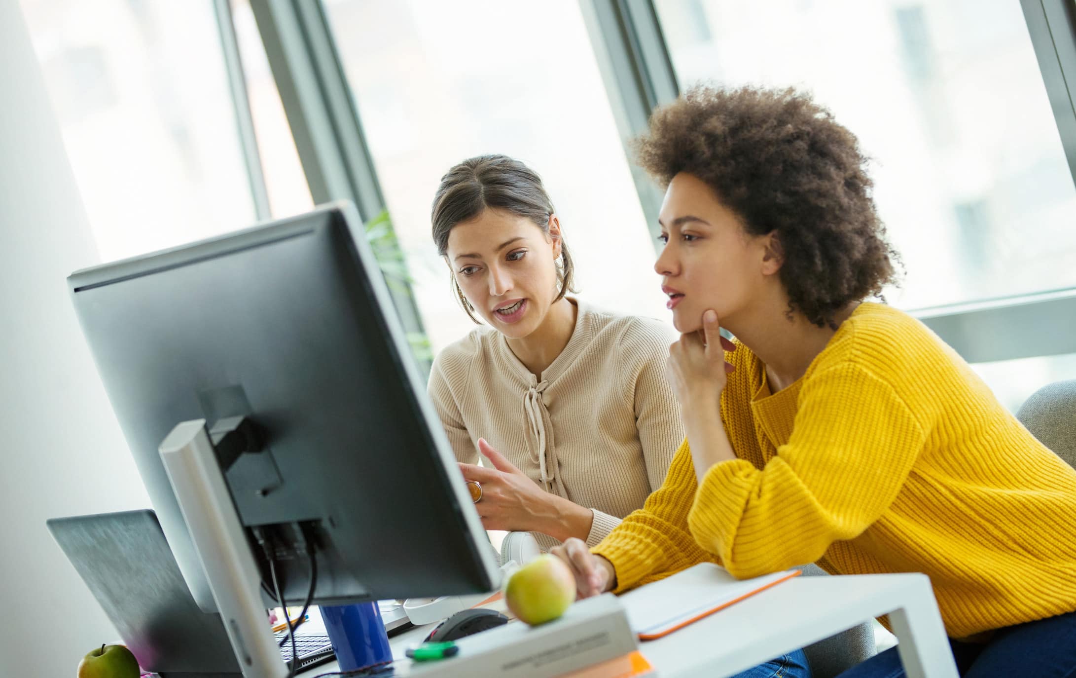 Two women collaborating at a computer in a bright office, focused on Law Firm Growth Advisory.