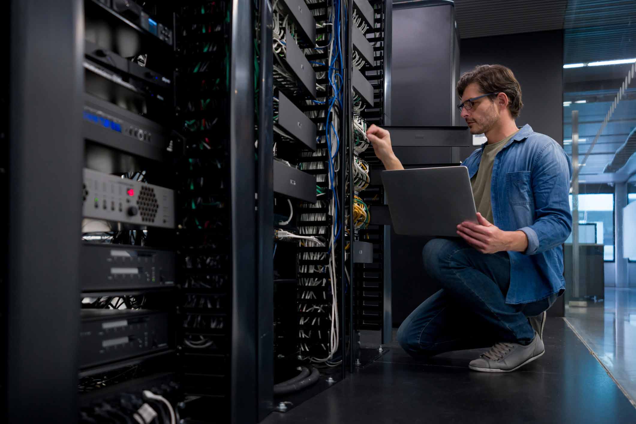 Man kneeling with laptop, working on cables in a server room for eDiscovery advisory.