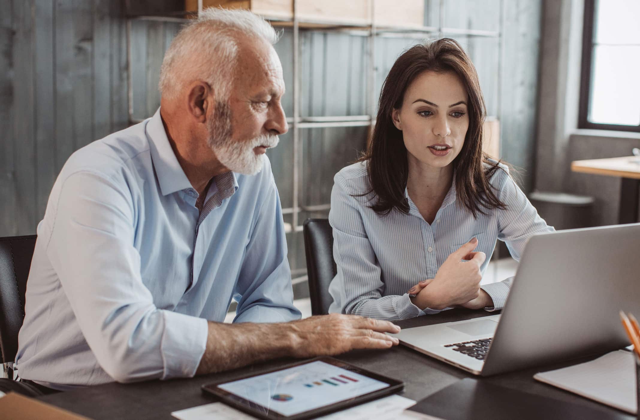 Older man and younger woman discussing business valuation while working at a laptop together.