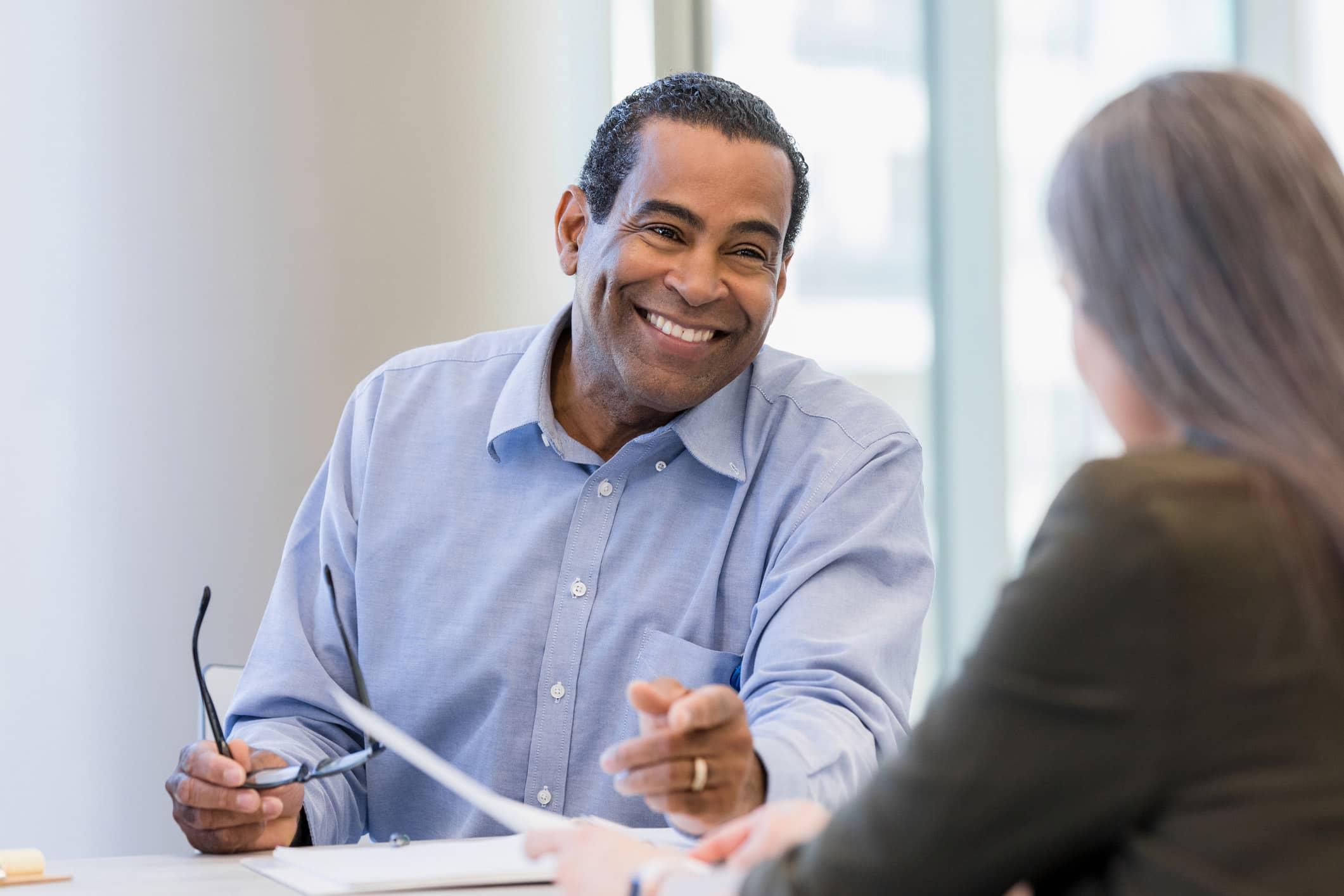 Smiling man holding glasses discusses law firm strategic planning models with a colleague.