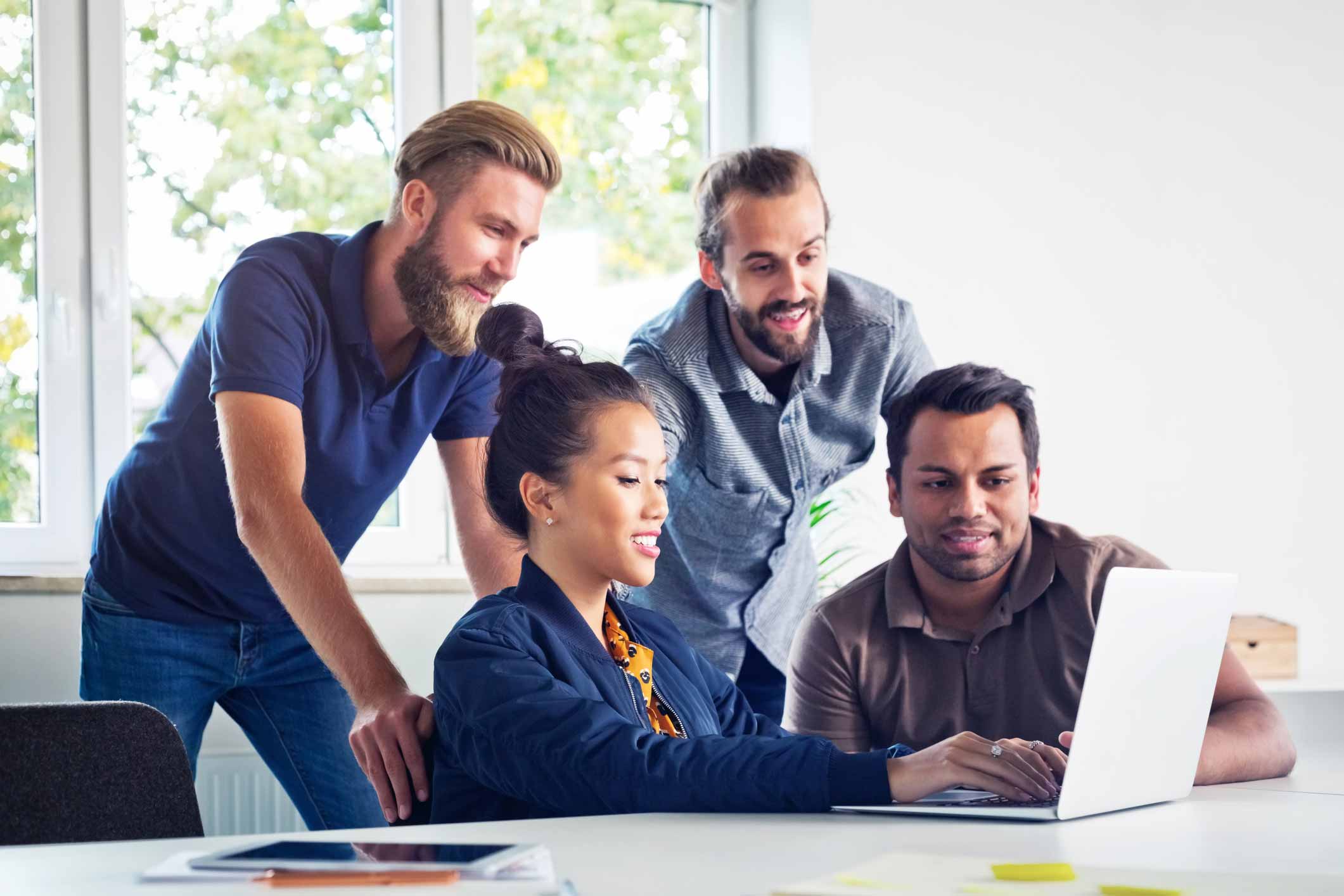 Four people collaborate around a laptop, exploring eDiscovery and automation in a bright office.