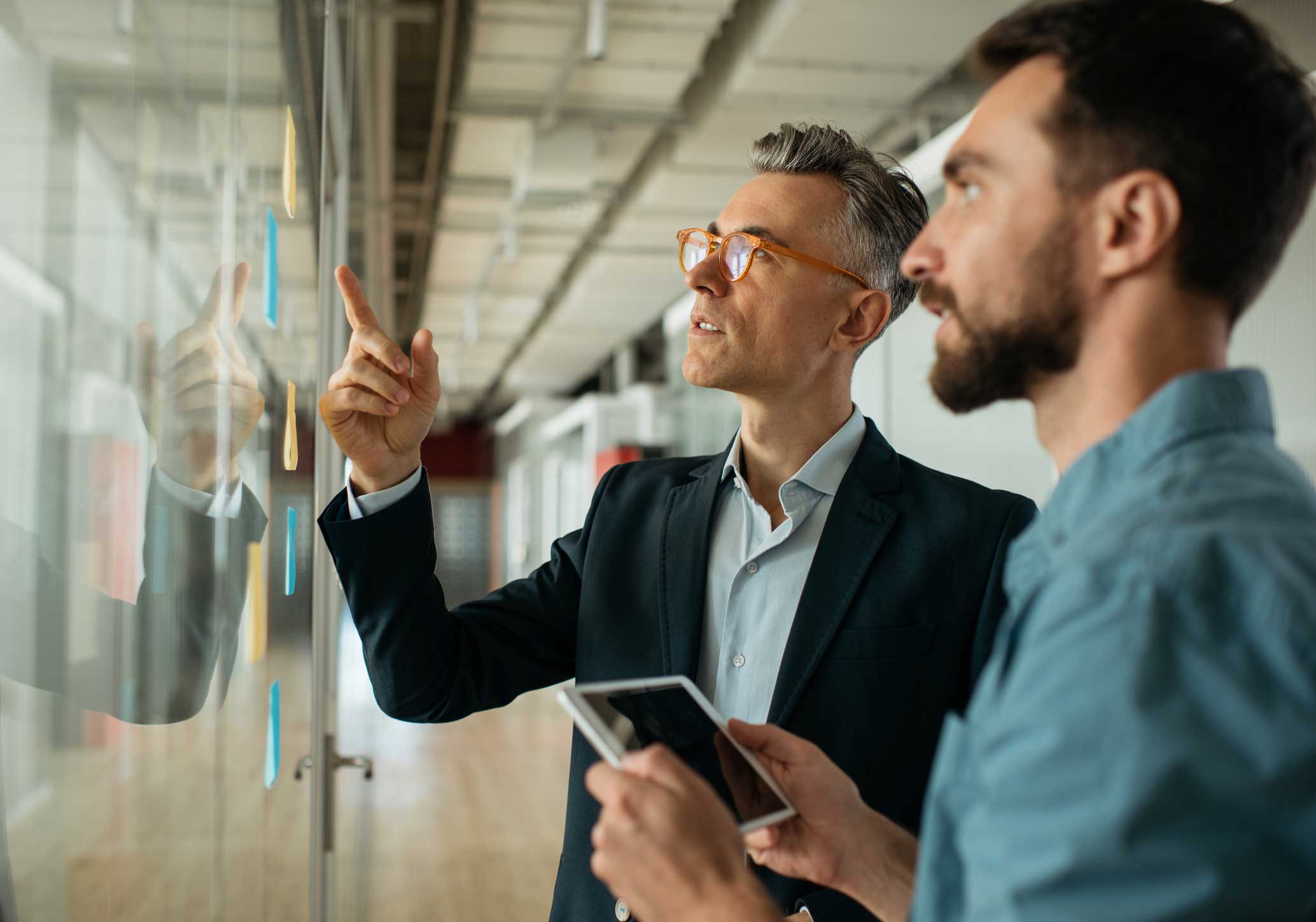 Two men discuss eDiscovery notes on a glass wall; one holds a tablet, consulting together.