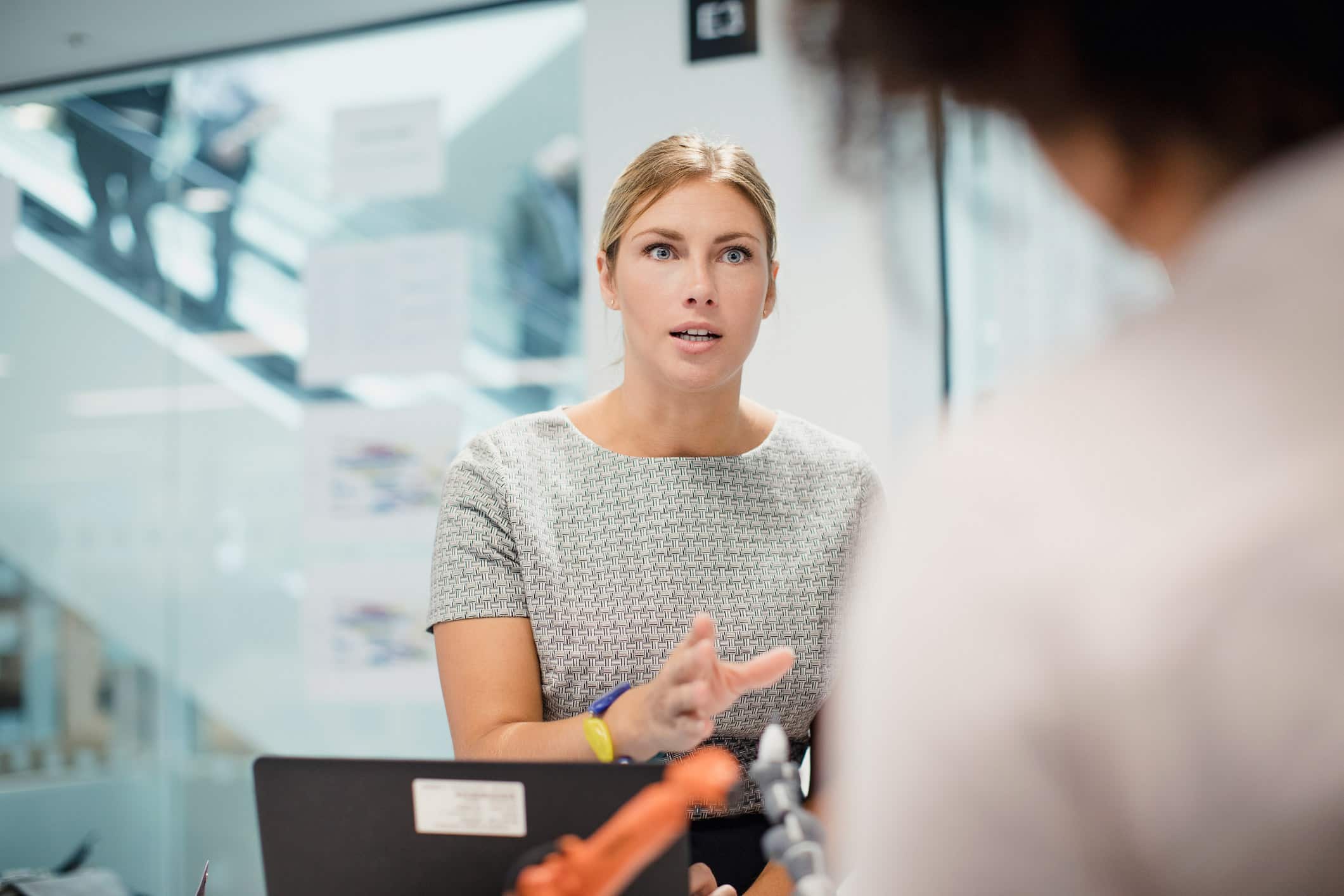 Woman in office discusses law firm strategic planning, gesturing near a laptop.