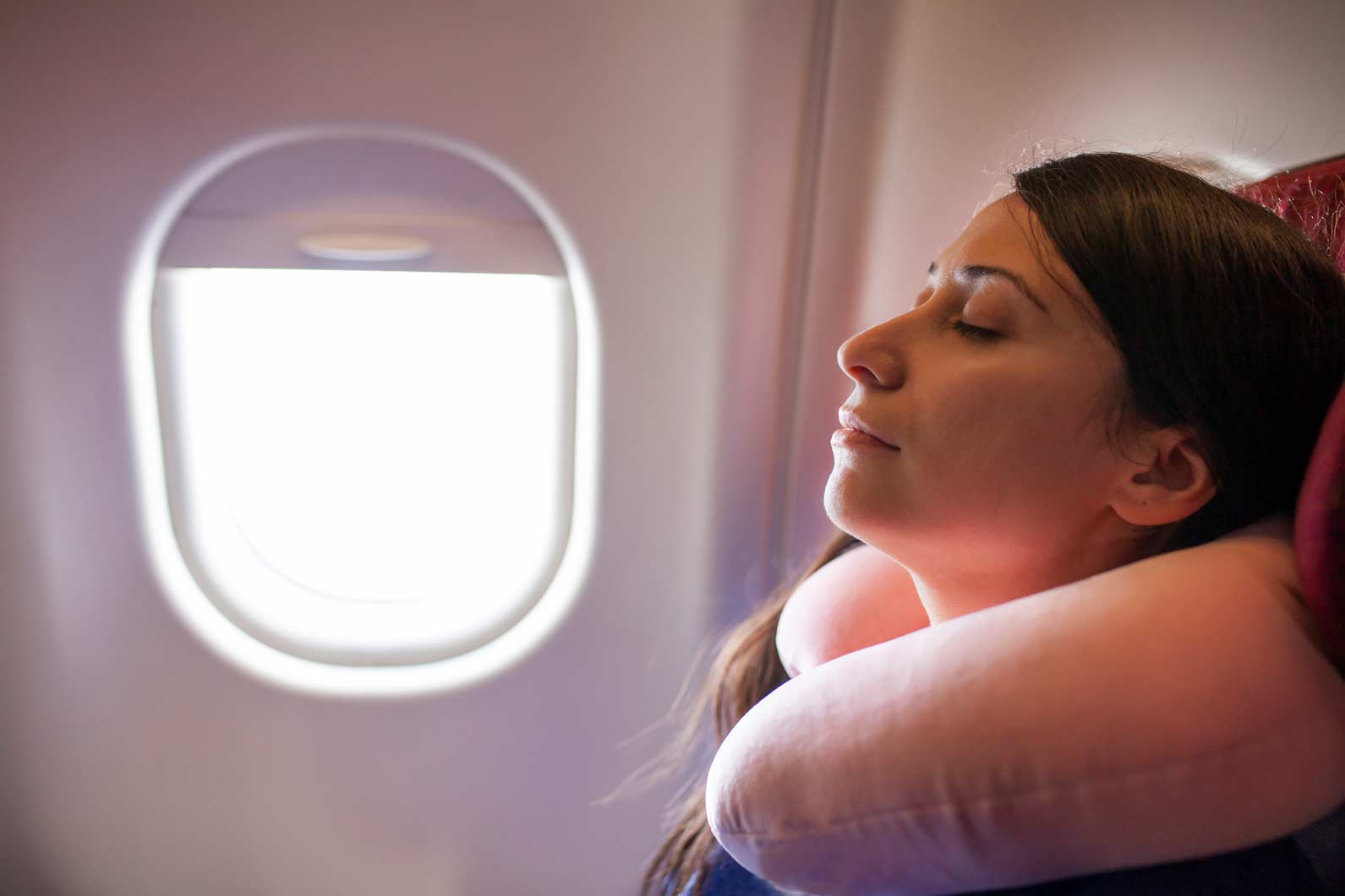 Woman with neck pillow sleeping by airplane window; AI-Driven Passenger Segmentation onboard.