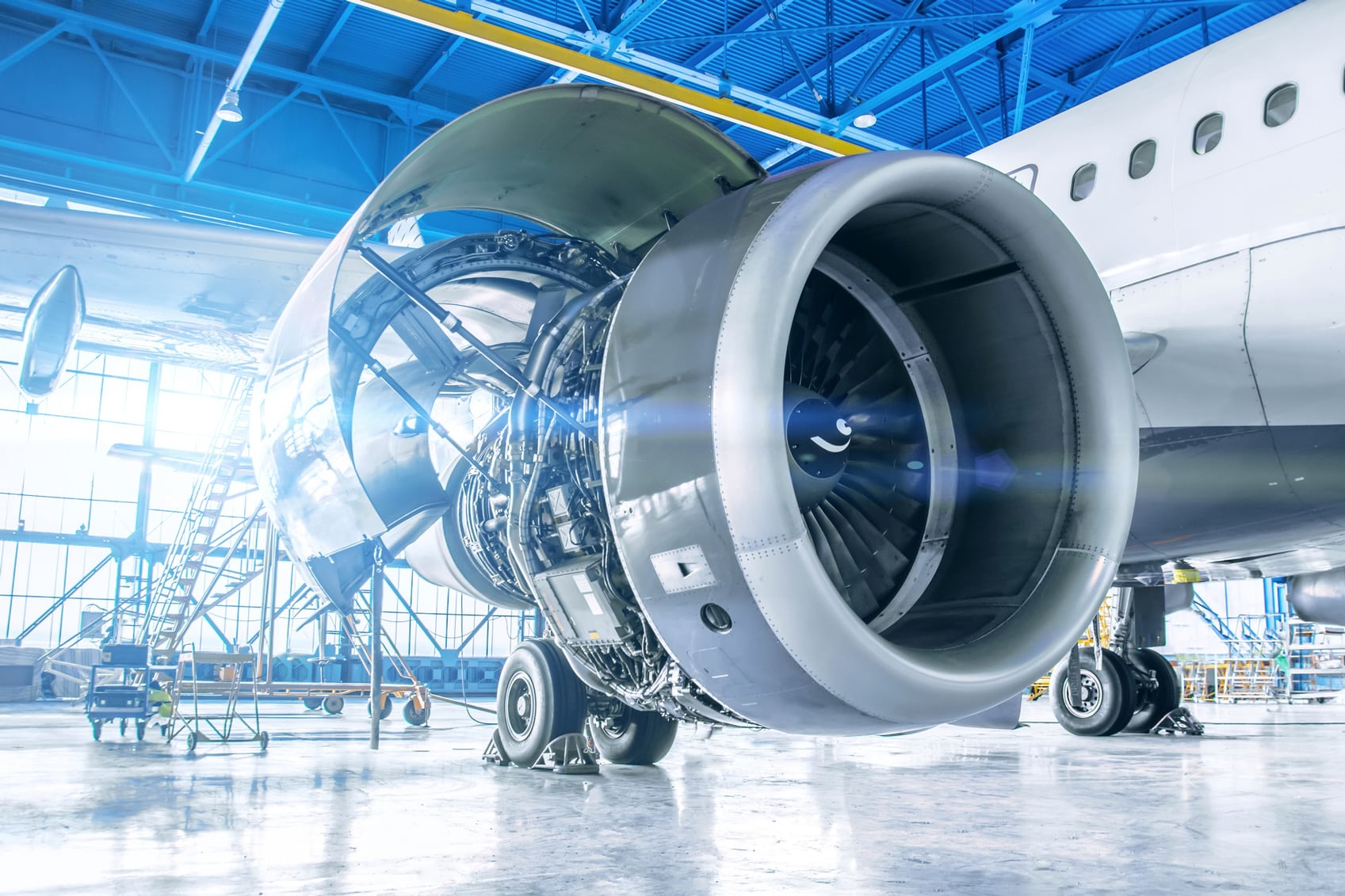 Close-up of Aircraft Maintenance & Engineering on a jet engine in a blue-ceilinged hangar.