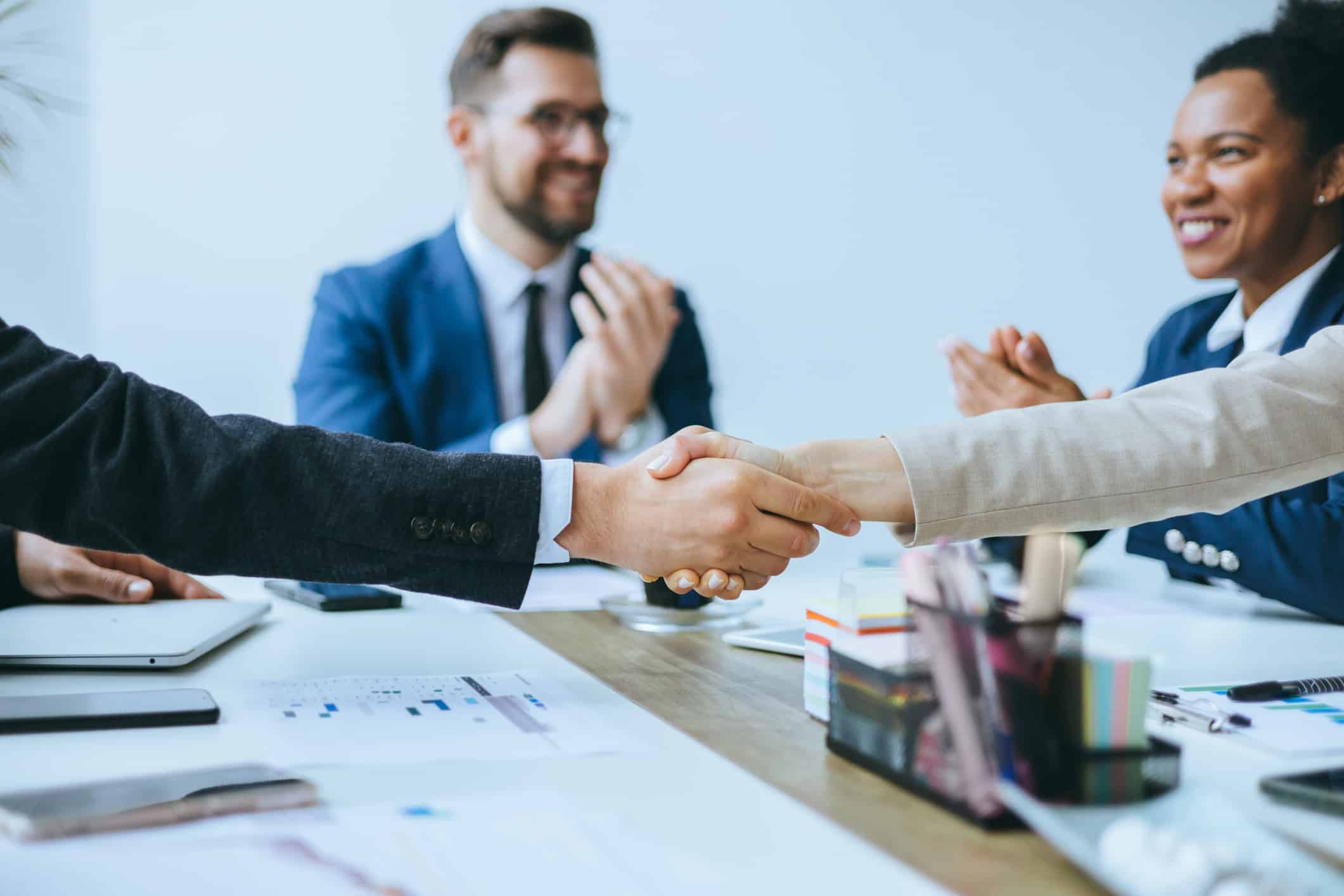 Two people shaking hands at a meeting table after discussing an airline alliance strategy.
