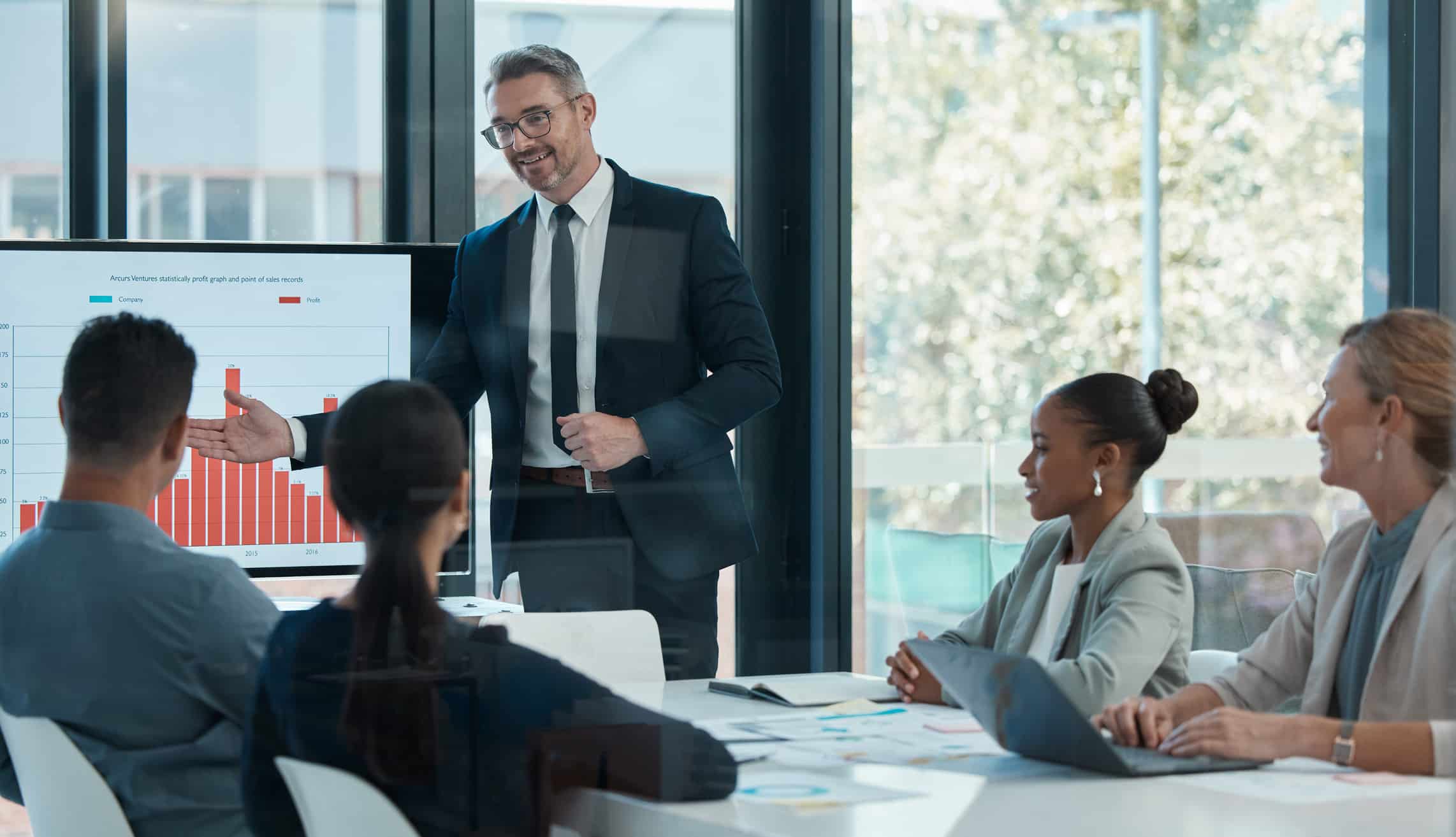 Man presenting a bar graph on aviation strategic planning consulting to 4 colleagues in a room.