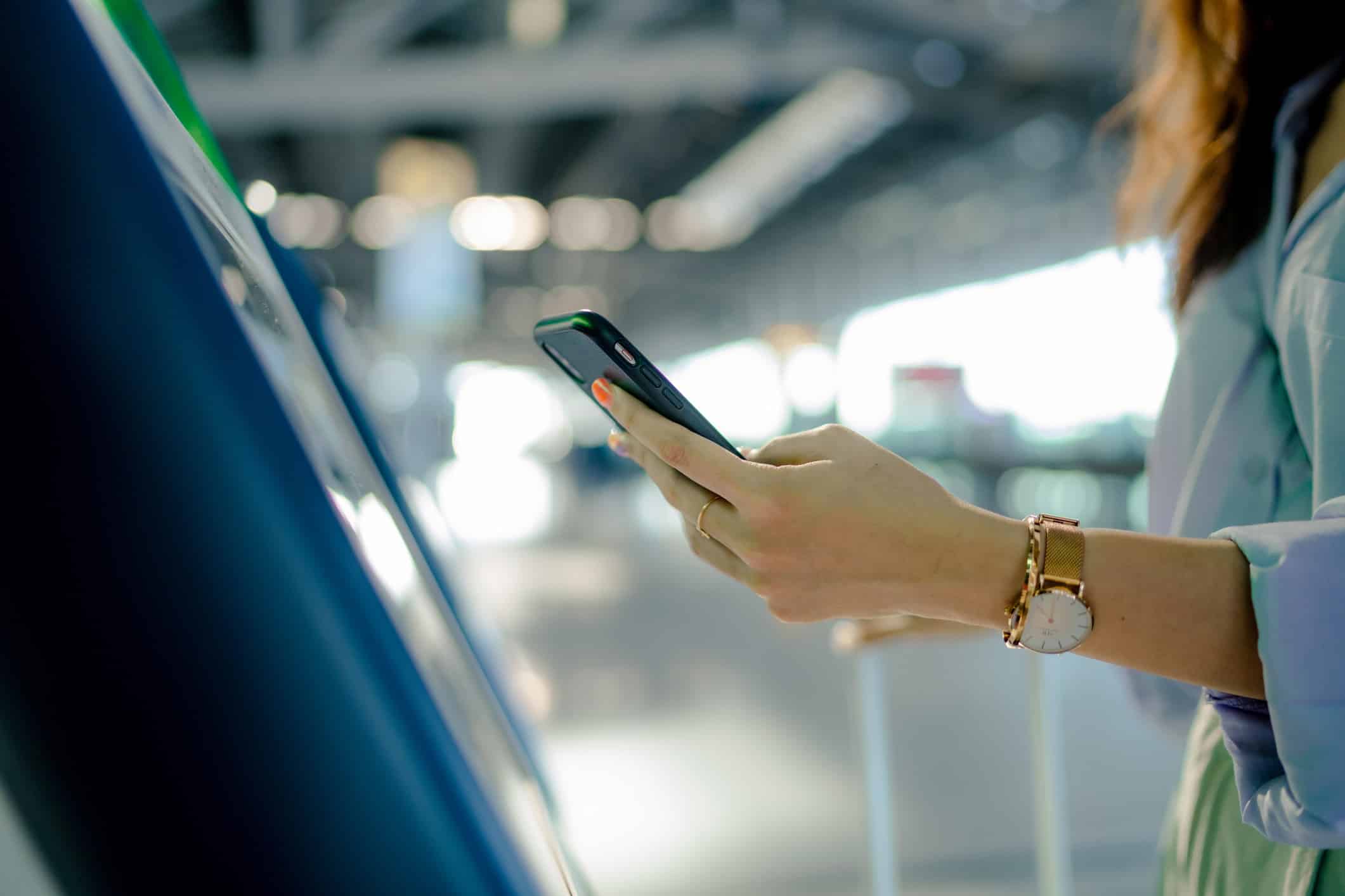 Woman using a smartphone at a touchscreen kiosk, showcasing Airport Smart Infrastructure Planning.