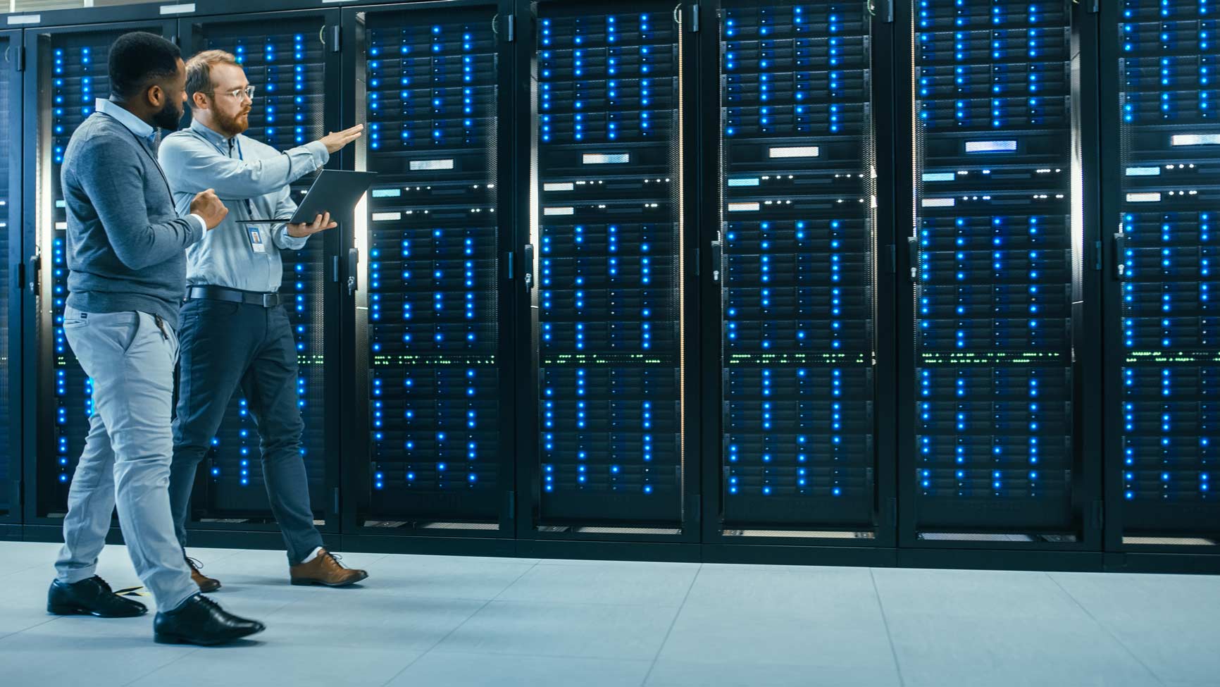 Two men discuss Aviation Cybersecurity in a server room with illuminated server racks.