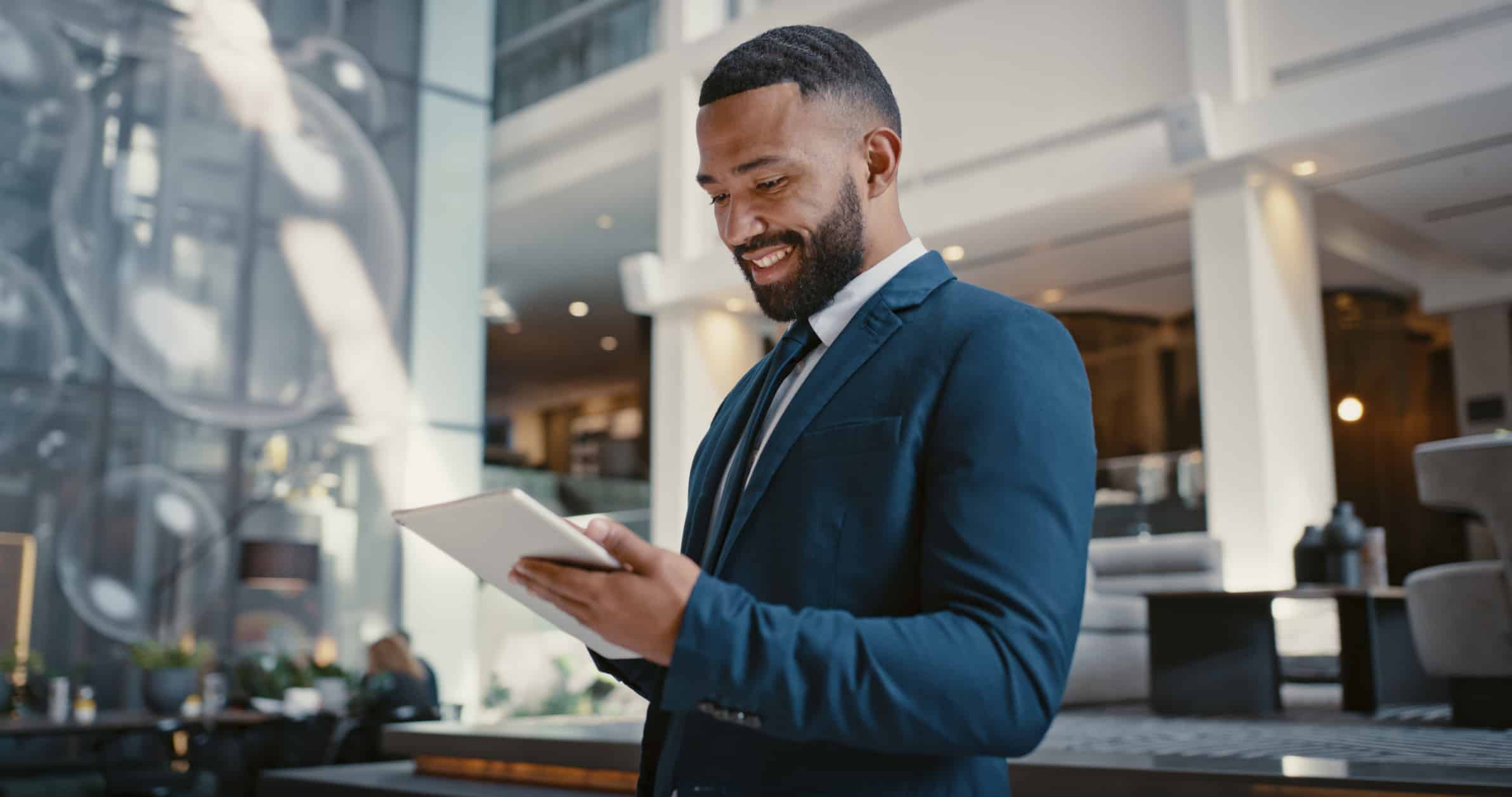 Smiling man using a tablet, exploring Hospitality AI Model Governance in bright office lobby.