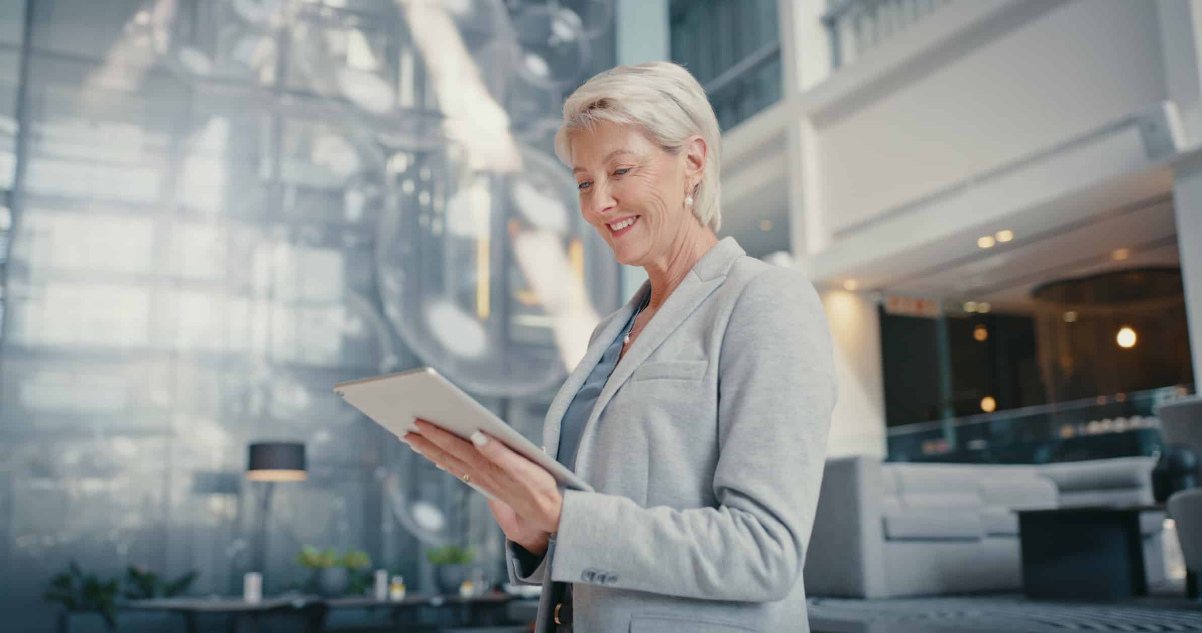 Smiling woman in a blazer using a tablet in an asset-light hospitality office lobby.