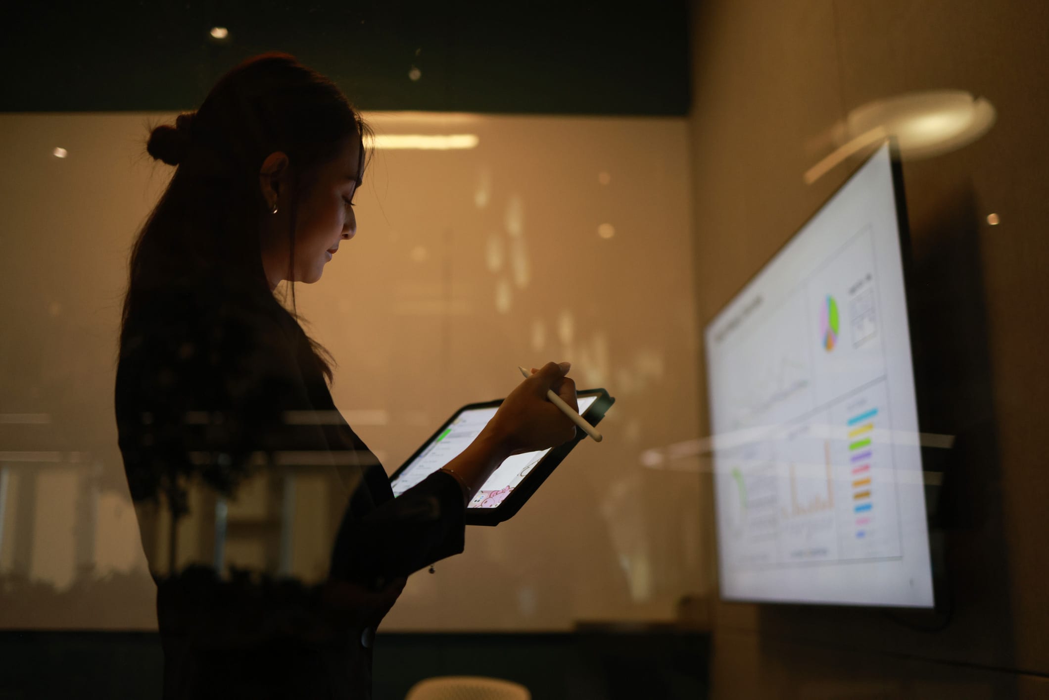 Woman using digital tablet in office, reviewing Hospitality Corporate Performance charts nearby.