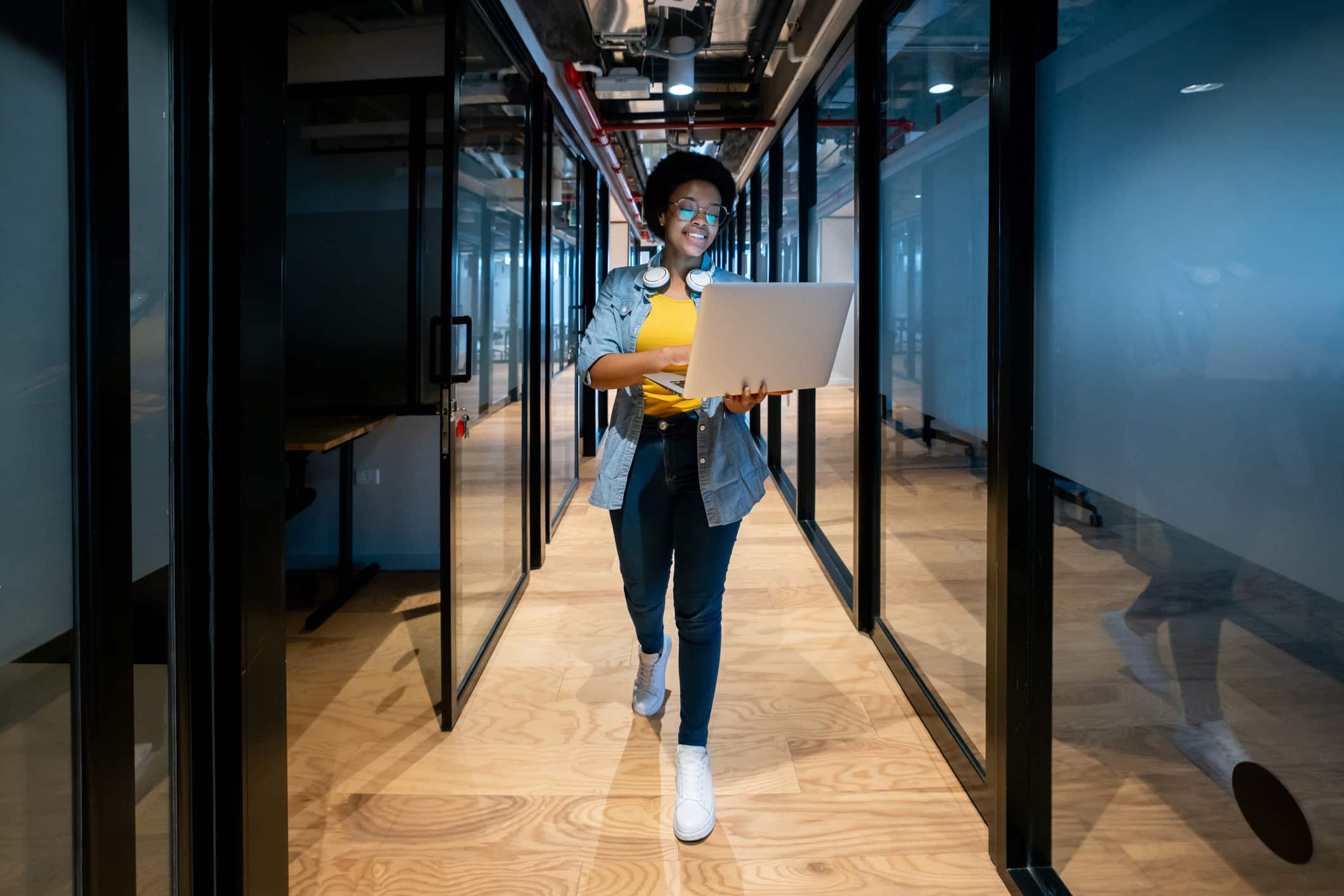 Smiling person in office hallway using a laptop for Hospitality Cloud-Based PMS & RMS Consulting.