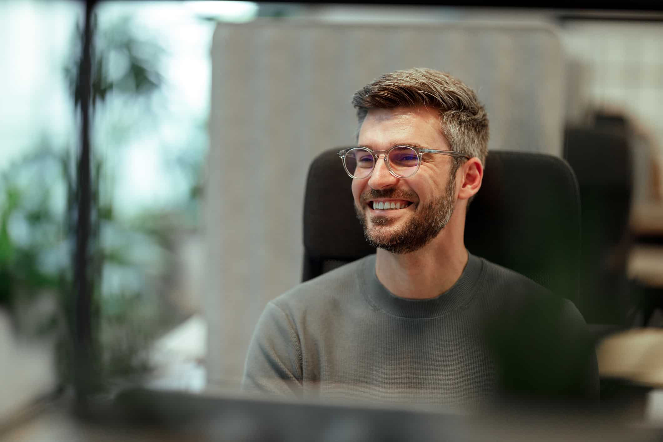 Smiling man with glasses sits at a desk, ready for Employer Value Proposition (EVP) consulting.