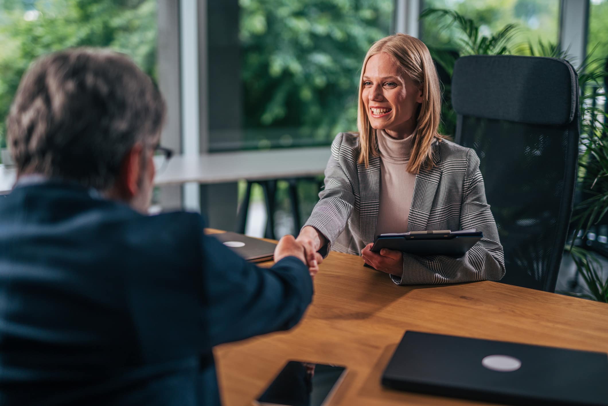 Woman in office shakes hands with man during Executive Search & Leadership Development meeting.