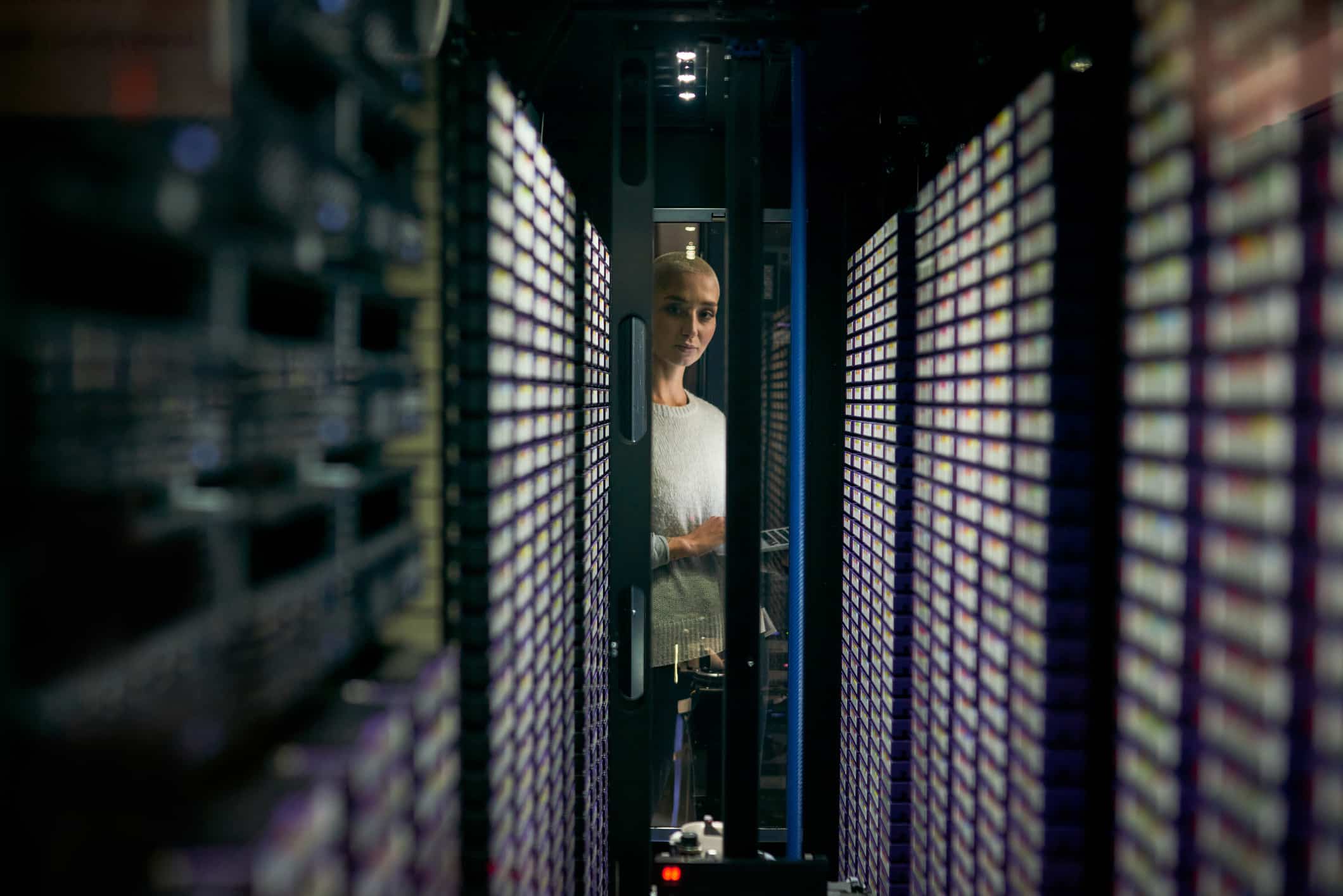 A woman stands between tall server racks, symbolizing cloud migration consulting expertise.