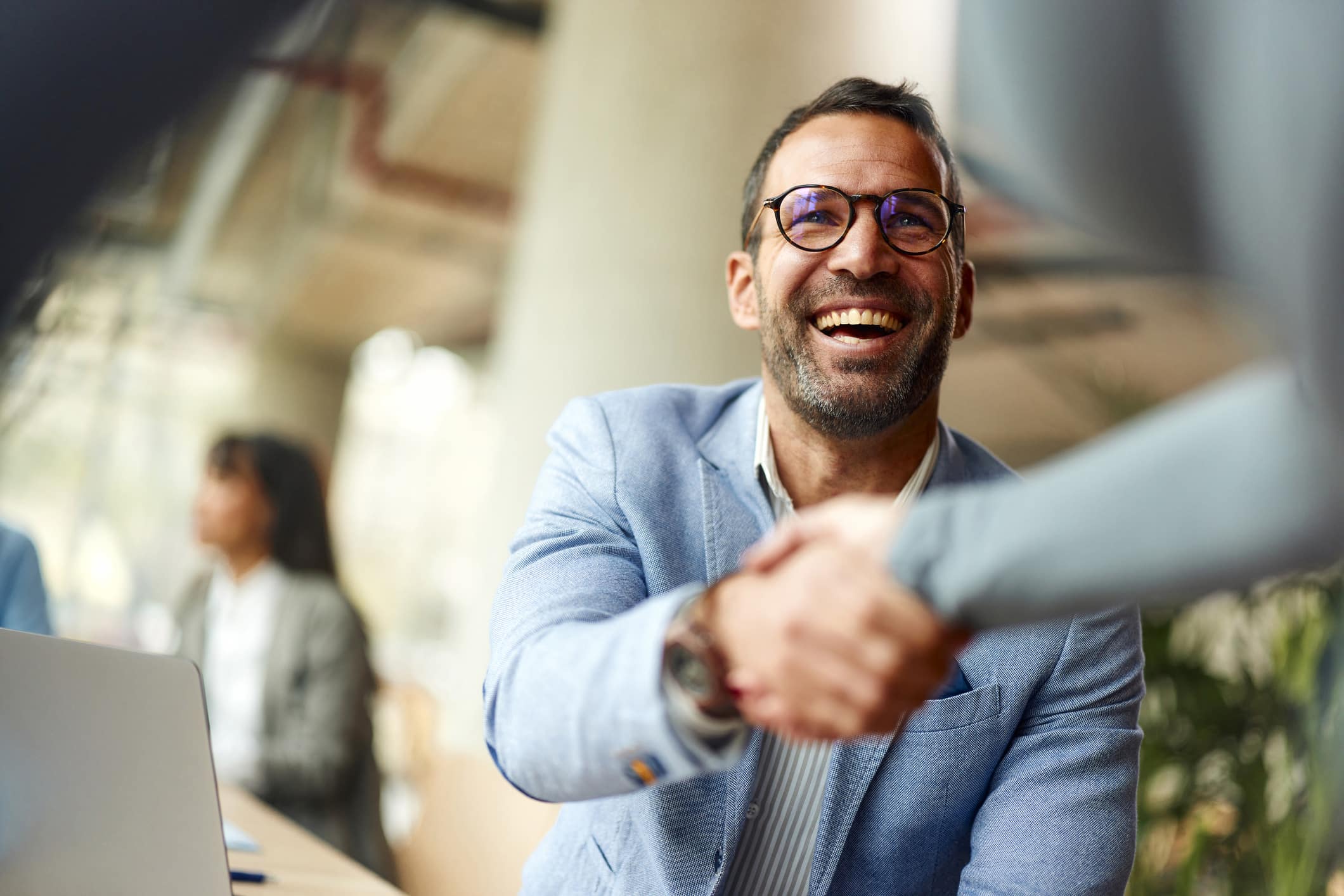 Smiling man in glasses shakes hands, discussing guest engagement strategy in an office setting.