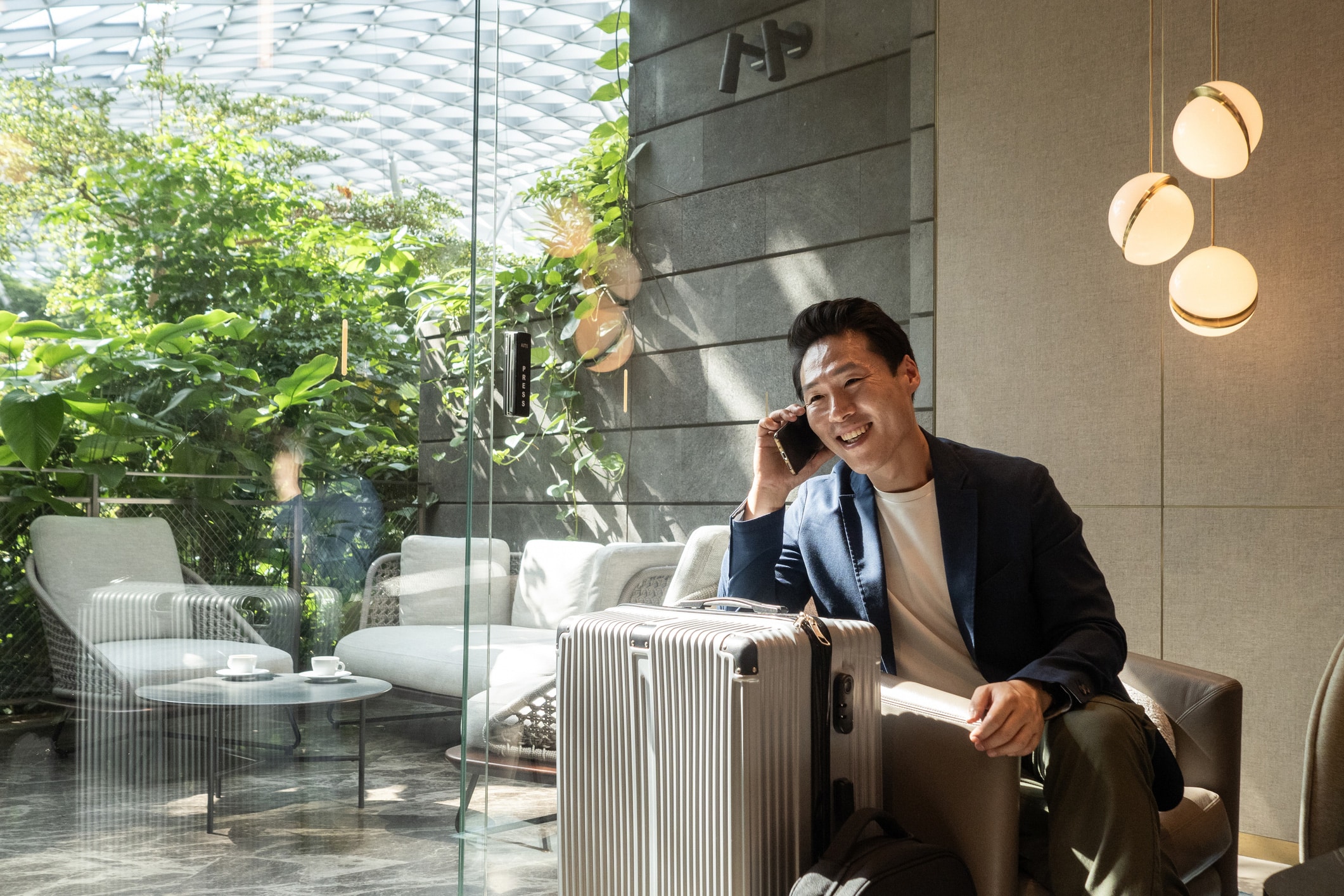 Man smiling on phone, enjoying omnichannel customer experience in a modern lounge with luggage.