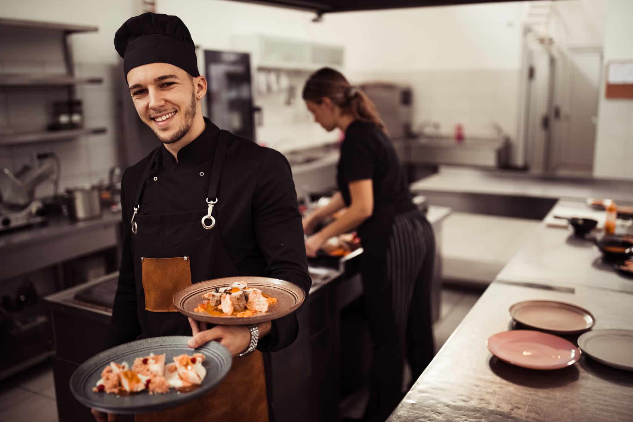 Smiling chef holding plates in a kitchen, embracing organizational change management.