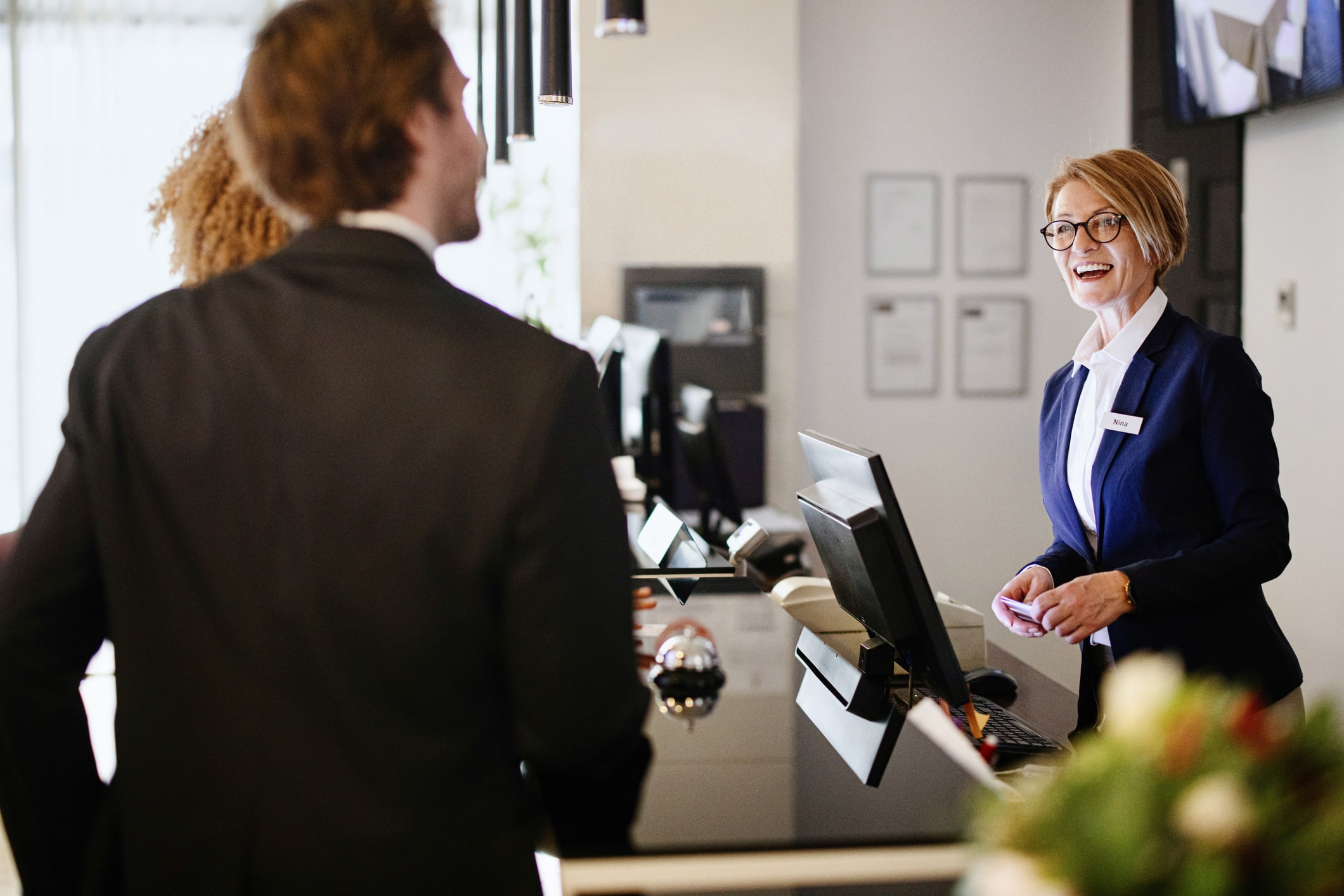Smiling receptionist assists a man in a suit at a luxury hospitality front desk.