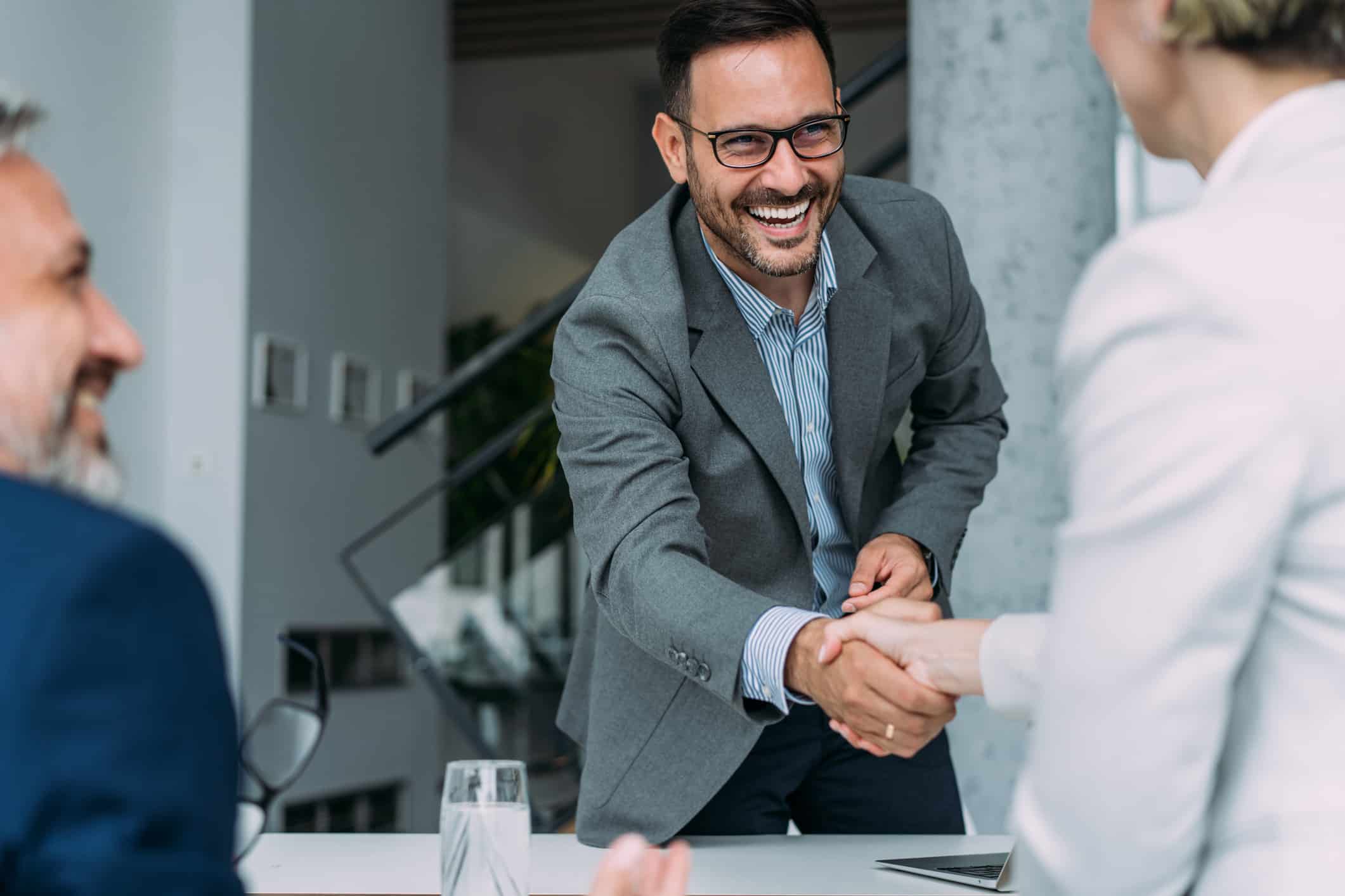 Smiling man in a suit shakes hands, reflecting service excellence in an office setting.