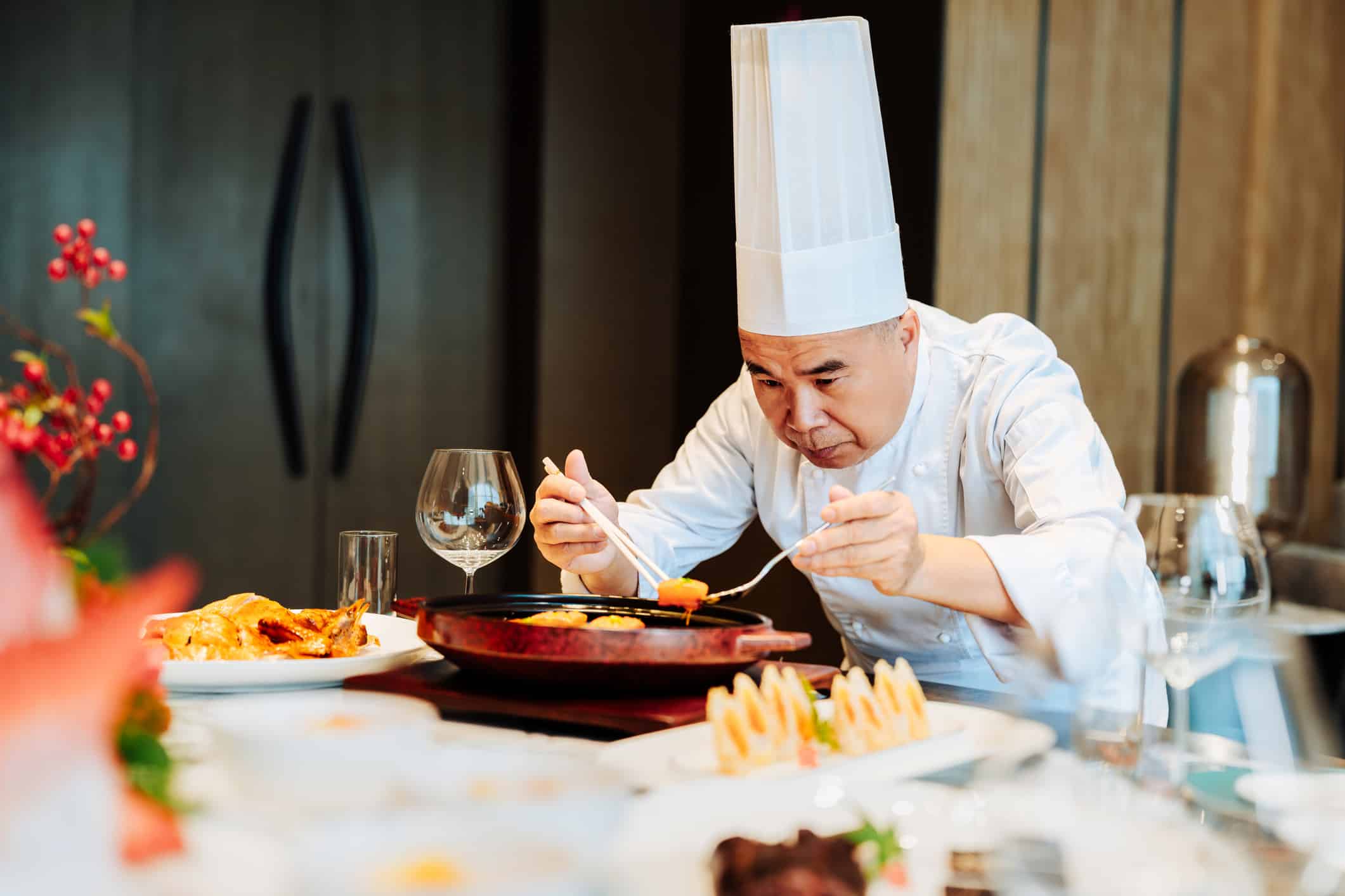 A chef in a tall white hat plating dishes, reflecting ultra-premium hospitality market strategy.