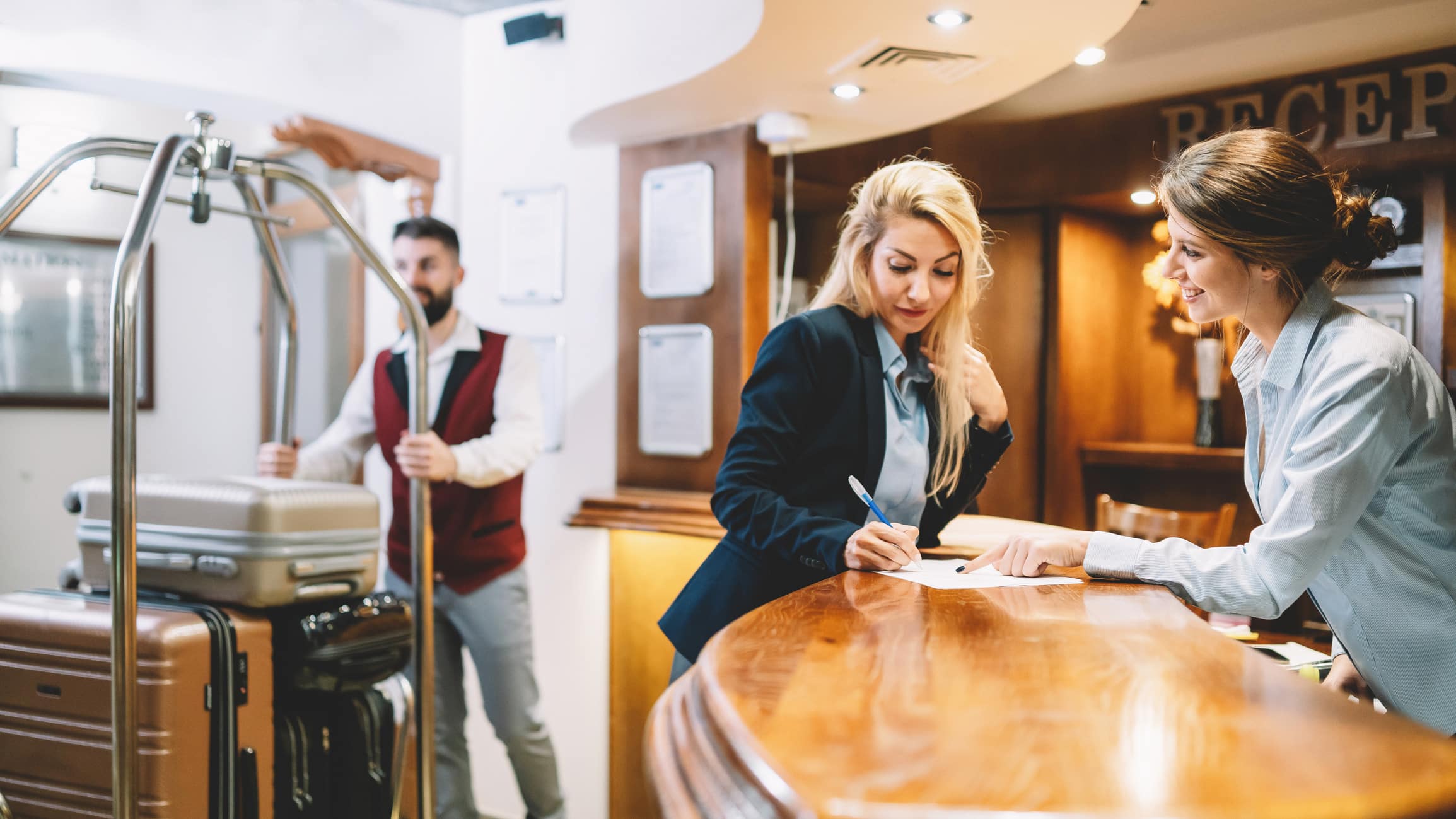 Two women check in at reception; a bellhop with luggage highlights NDC innovation for hospitality.