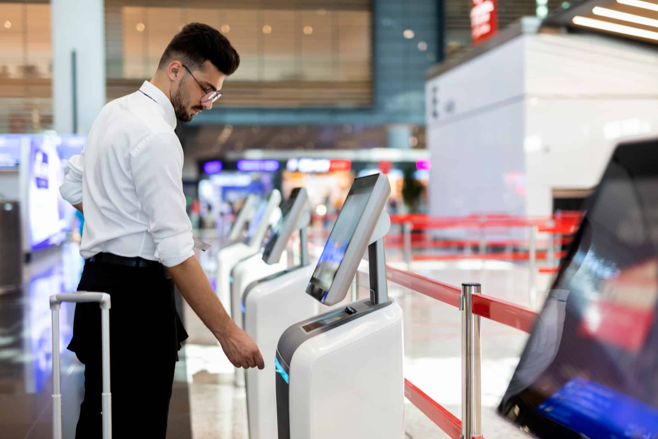 Man using a self-service kiosk at airport, suitcase at his side, showcasing operational efficiency.