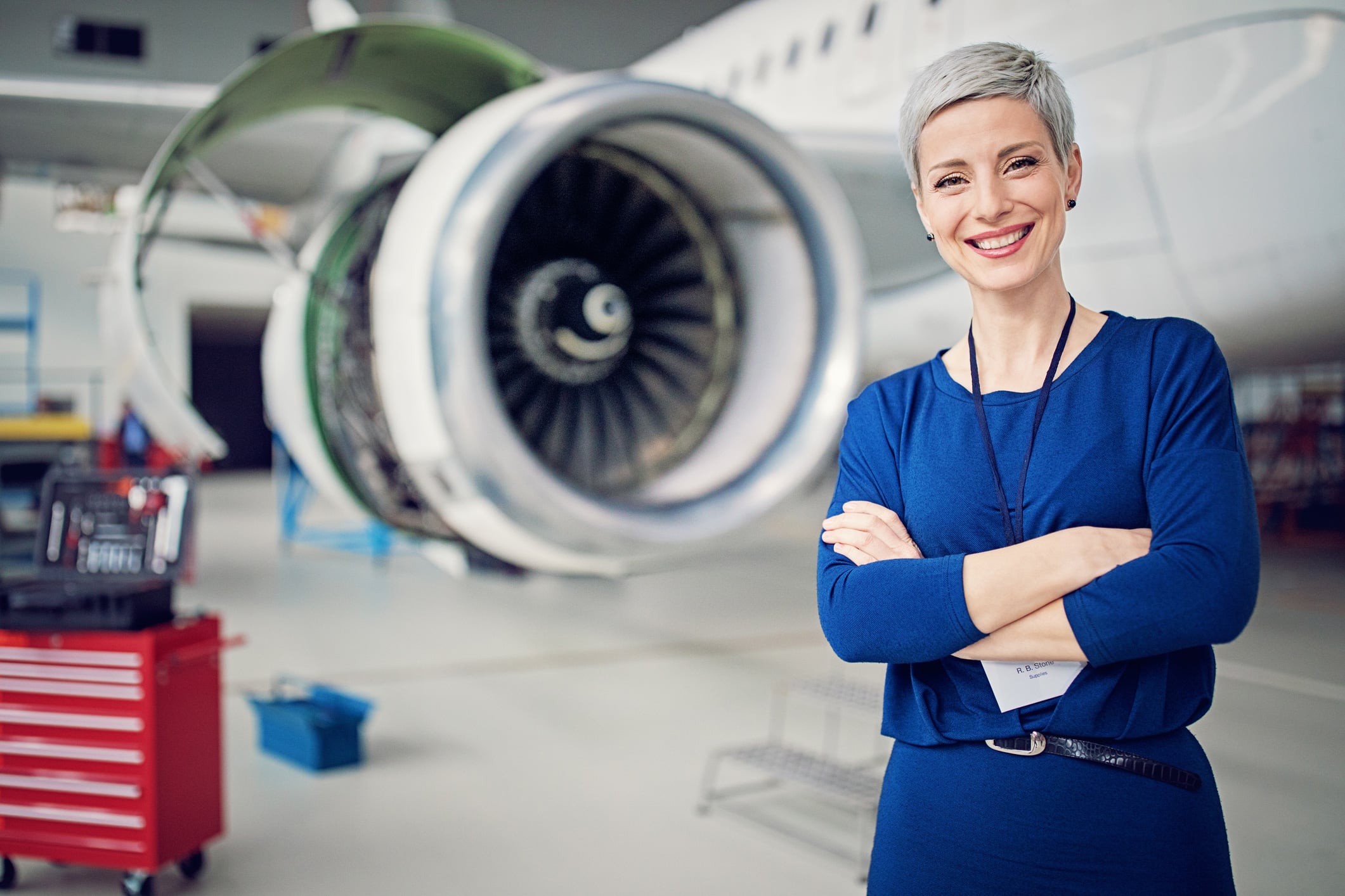 Woman in blue stands smiling, embodying succession planning before an airplane engine in a hangar.