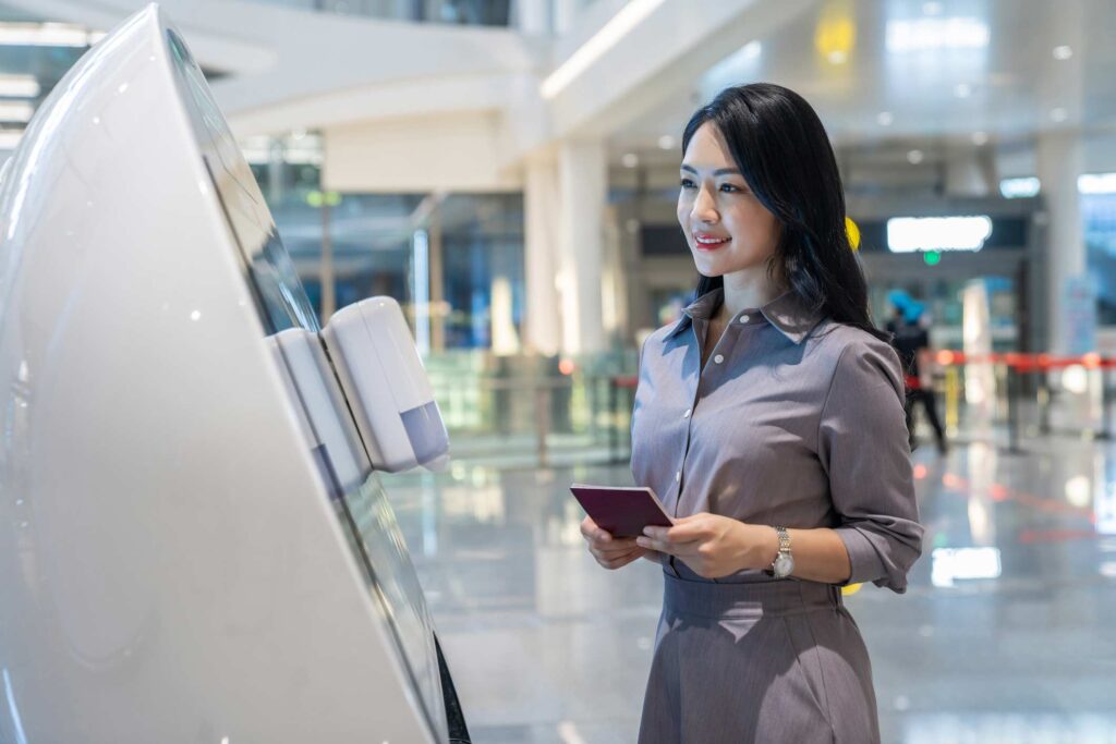 Woman with a passport smiles at airport kiosk, embracing aviation digital transformation consulting.