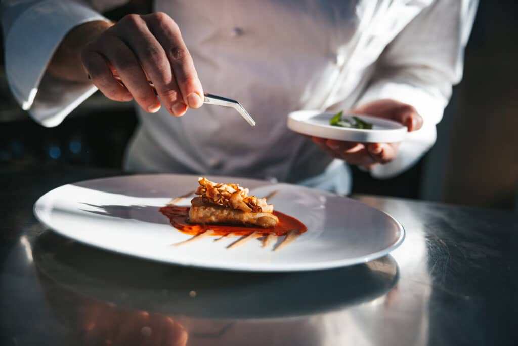 A chef garnishes a plated dish with tweezers, adding final touches to an elegant meal.