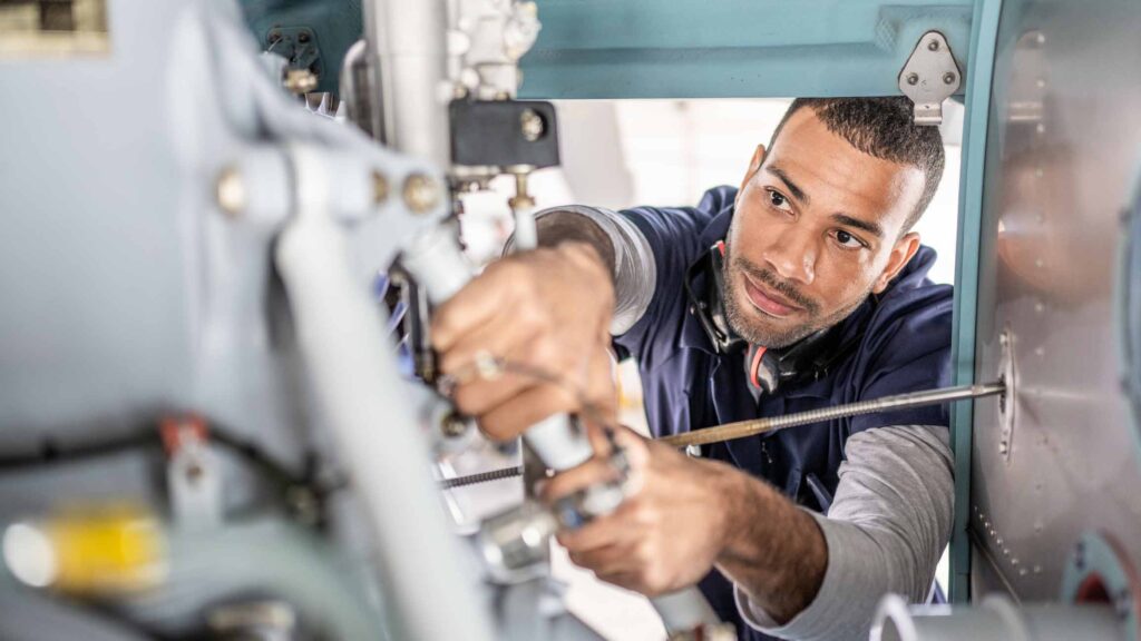 Man repairing machinery with precision, using tools in an industrial aviation consulting setting.