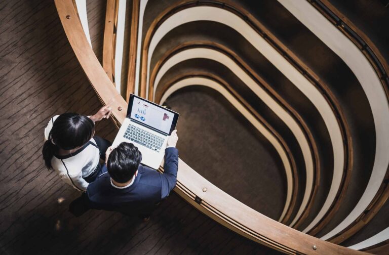 Two people review hospitality strategy innovation consulting charts on a laptop in a modern building