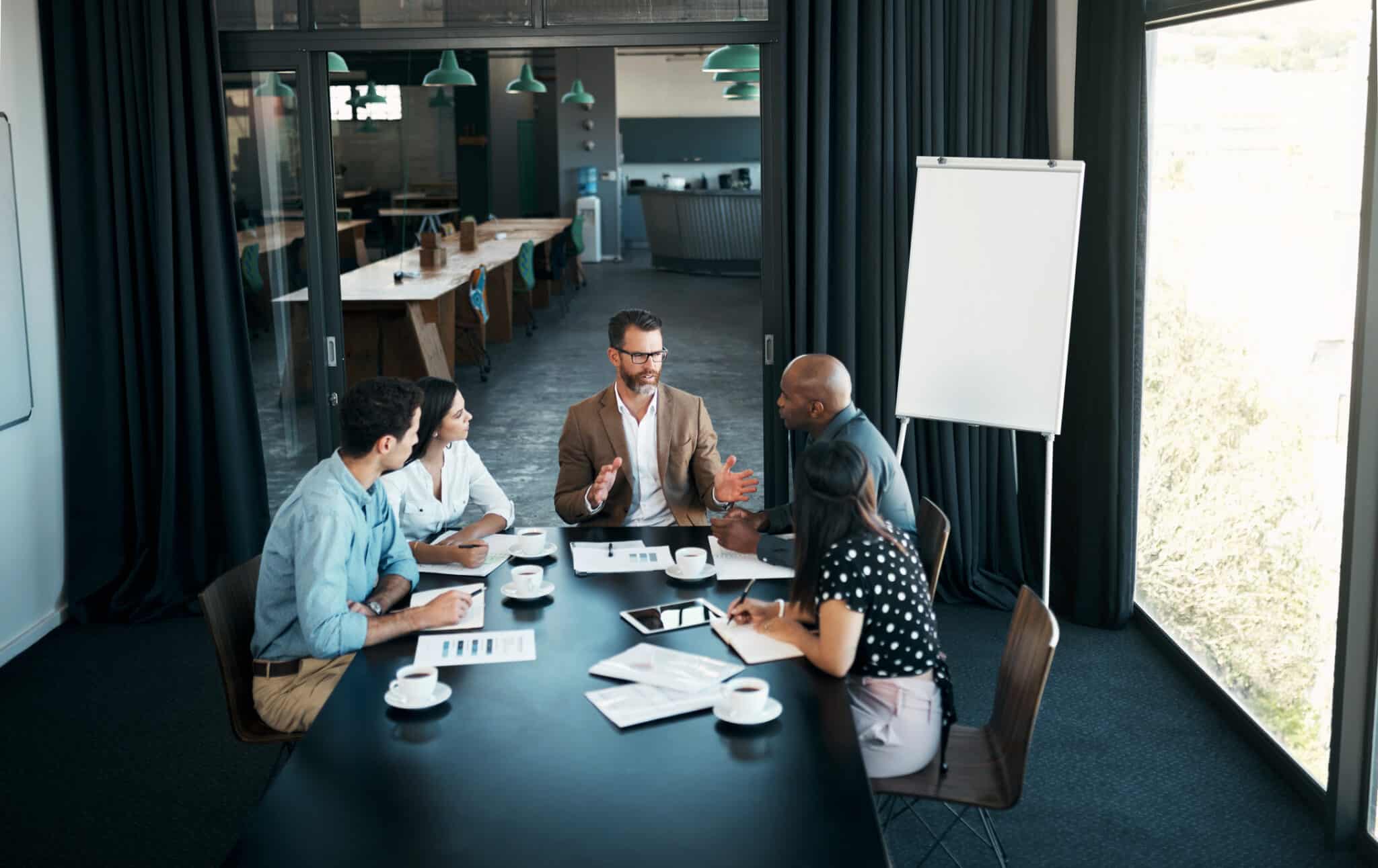 Five people having a discussion around a conference table with papers and coffee cups.