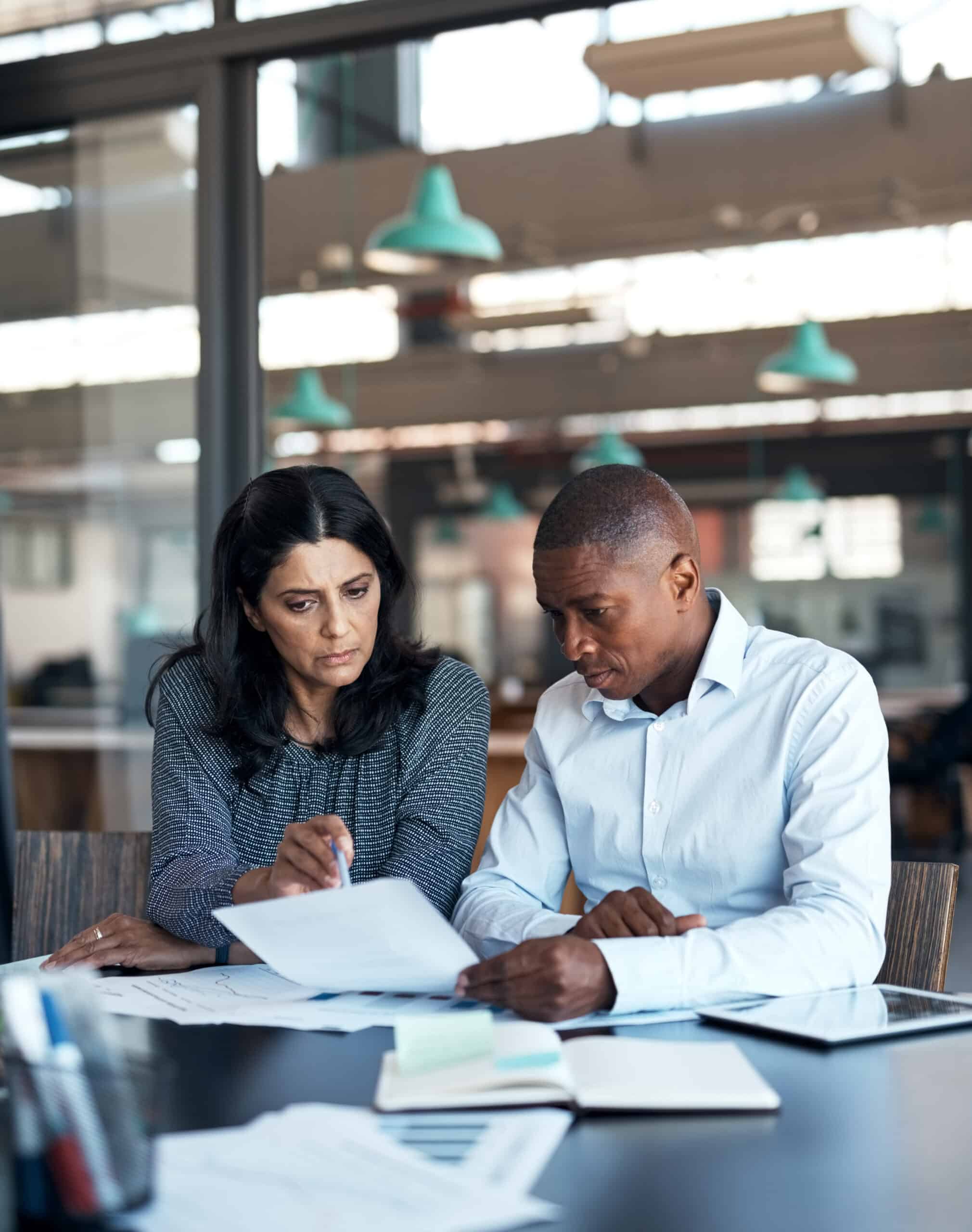 Two people sit at a desk reviewing documents on artificial intelligence consulting in a modern office.