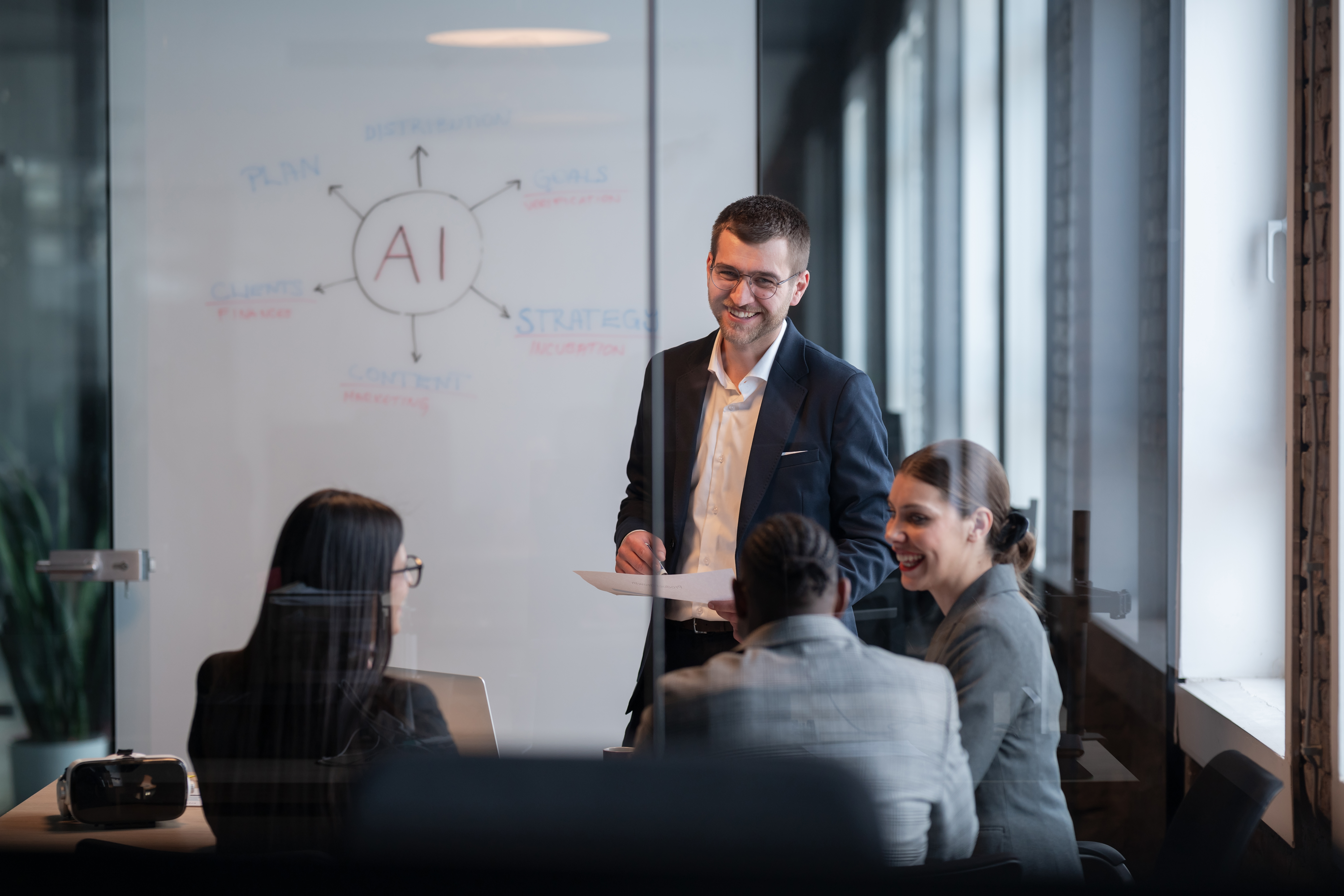 Four people in a meeting room discussing ai governance, with a whiteboard diagram behind them.