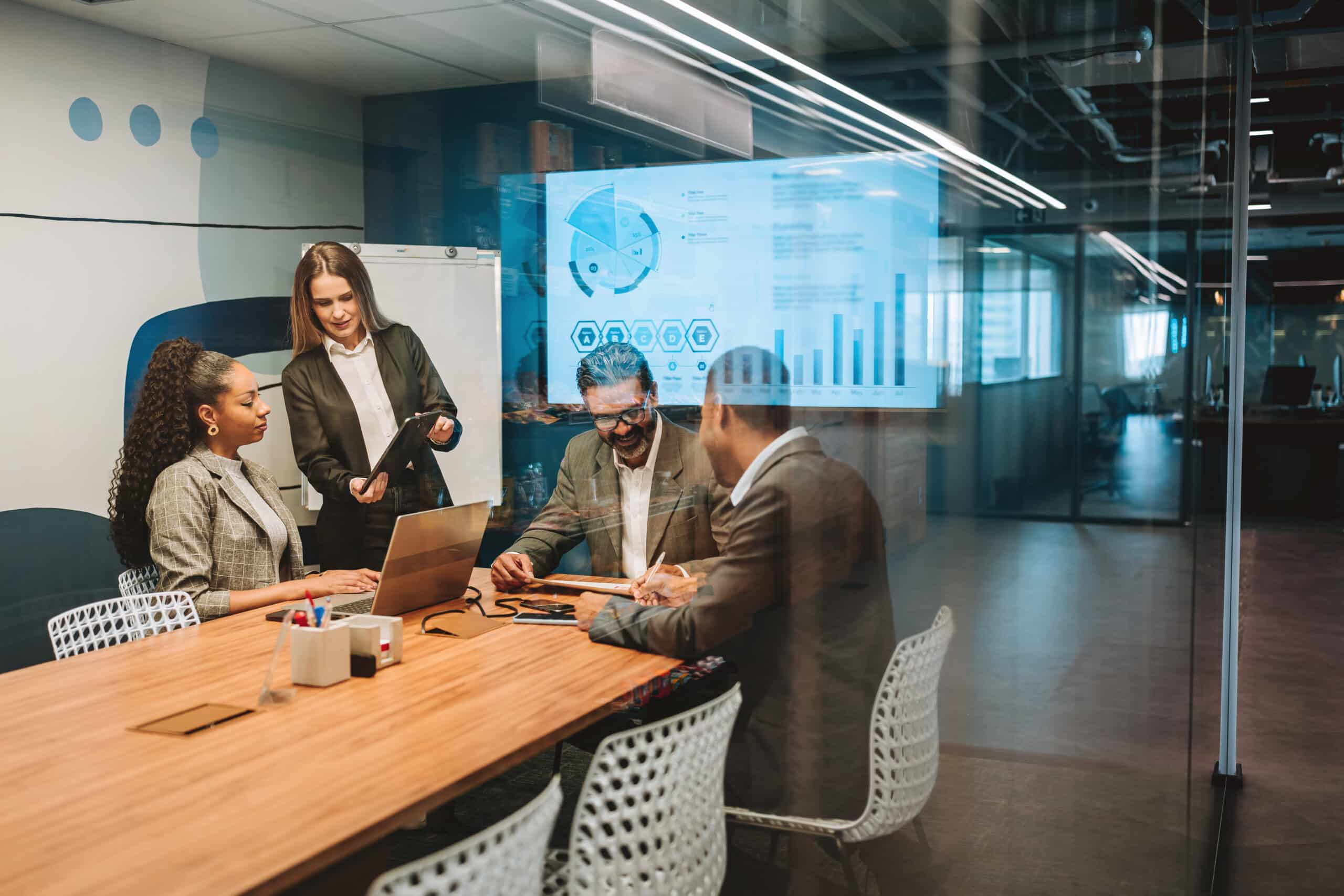 Four people in a meeting room discuss data with AI governance consultants on screen.