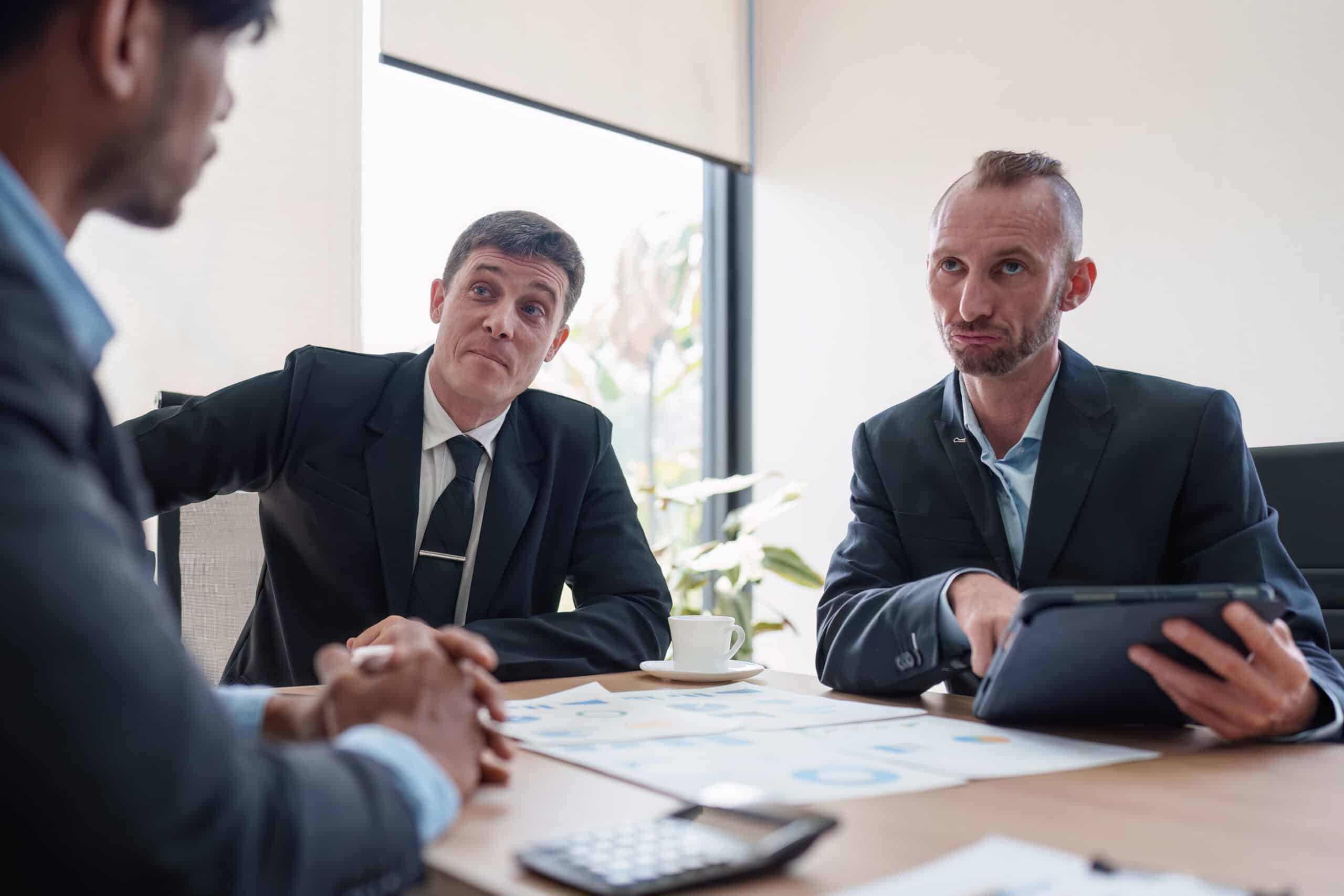 Three men in suits discuss documents and a tablet during an ai governance consulting session.
