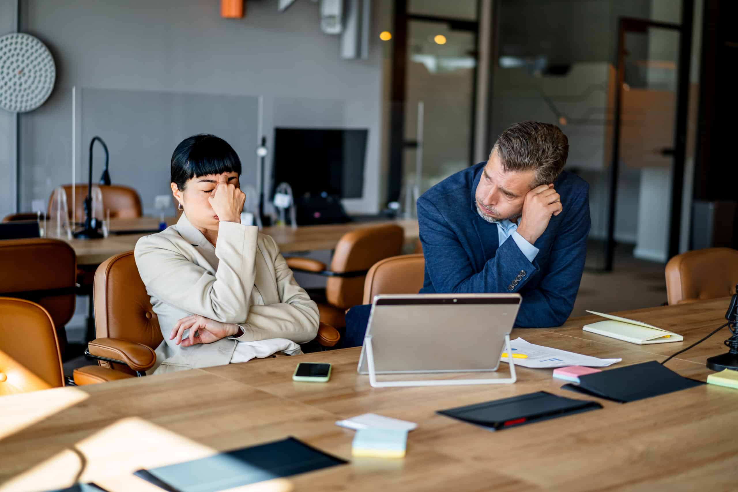 Two frustrated coworkers discuss ai governance consulting at a cluttered office desk.