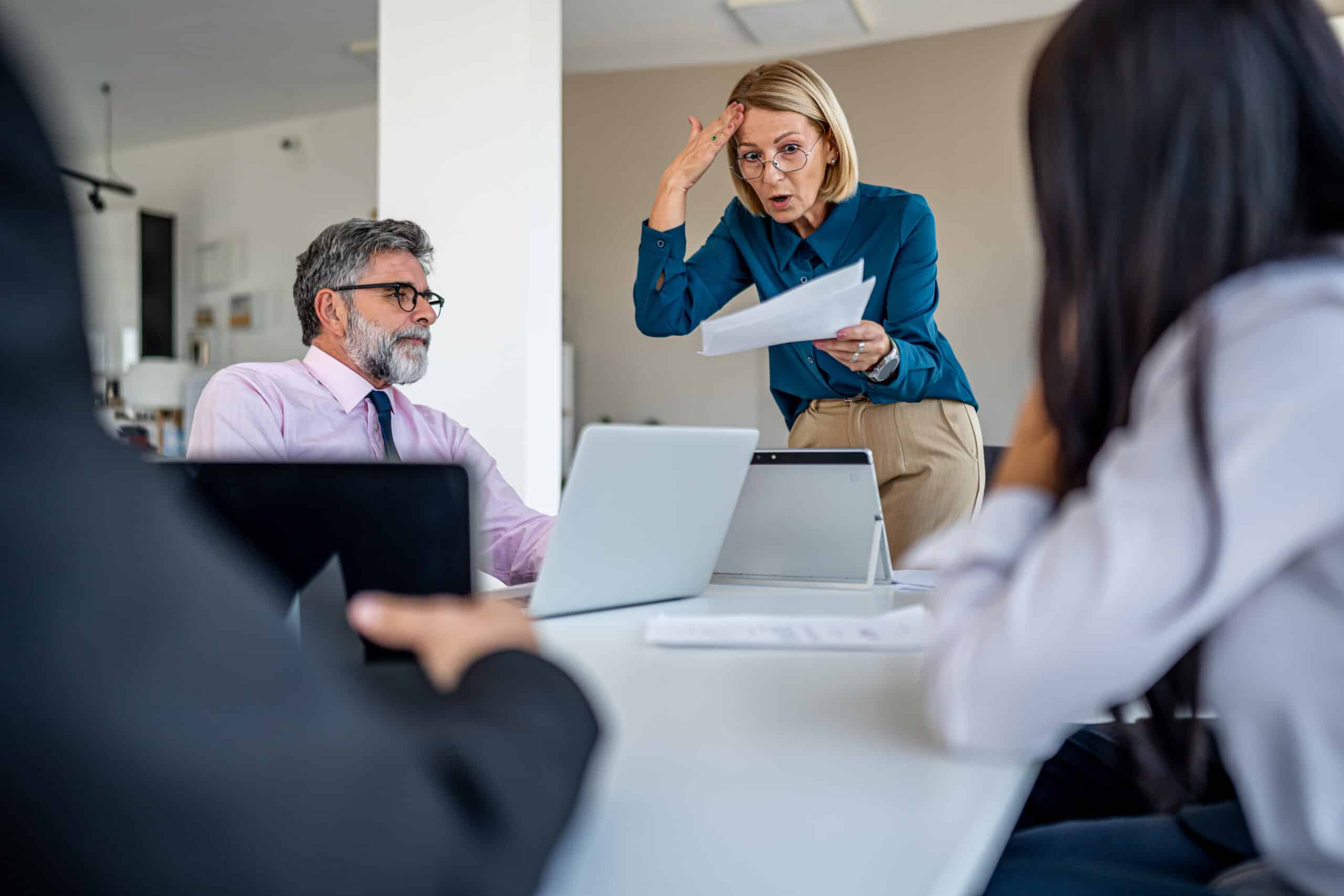 Woman holding papers appears frustrated while discussing ai governance with colleagues in a meeting room.