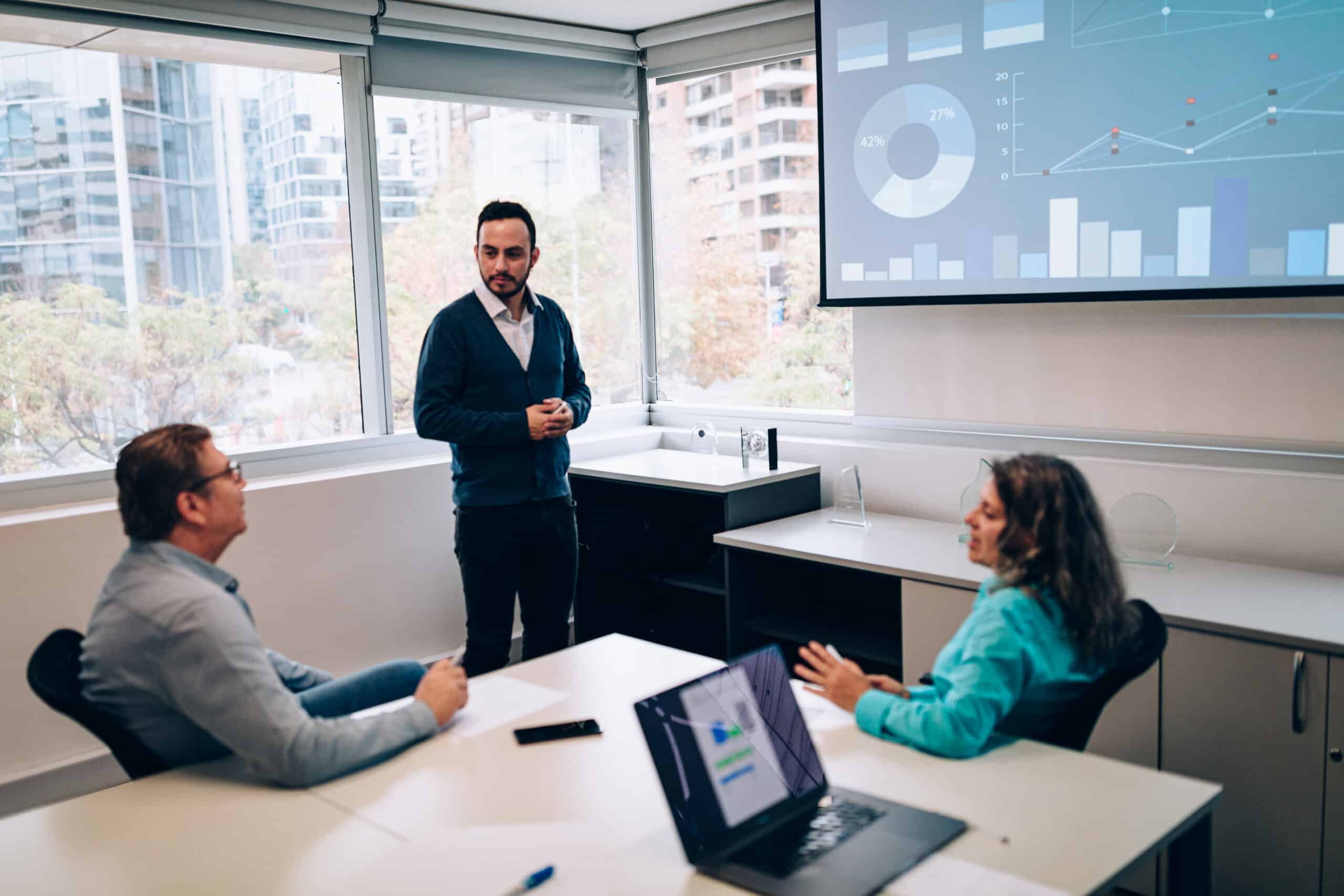 Three people in a meeting room discuss commercial real estate expansion strategy consulting.
