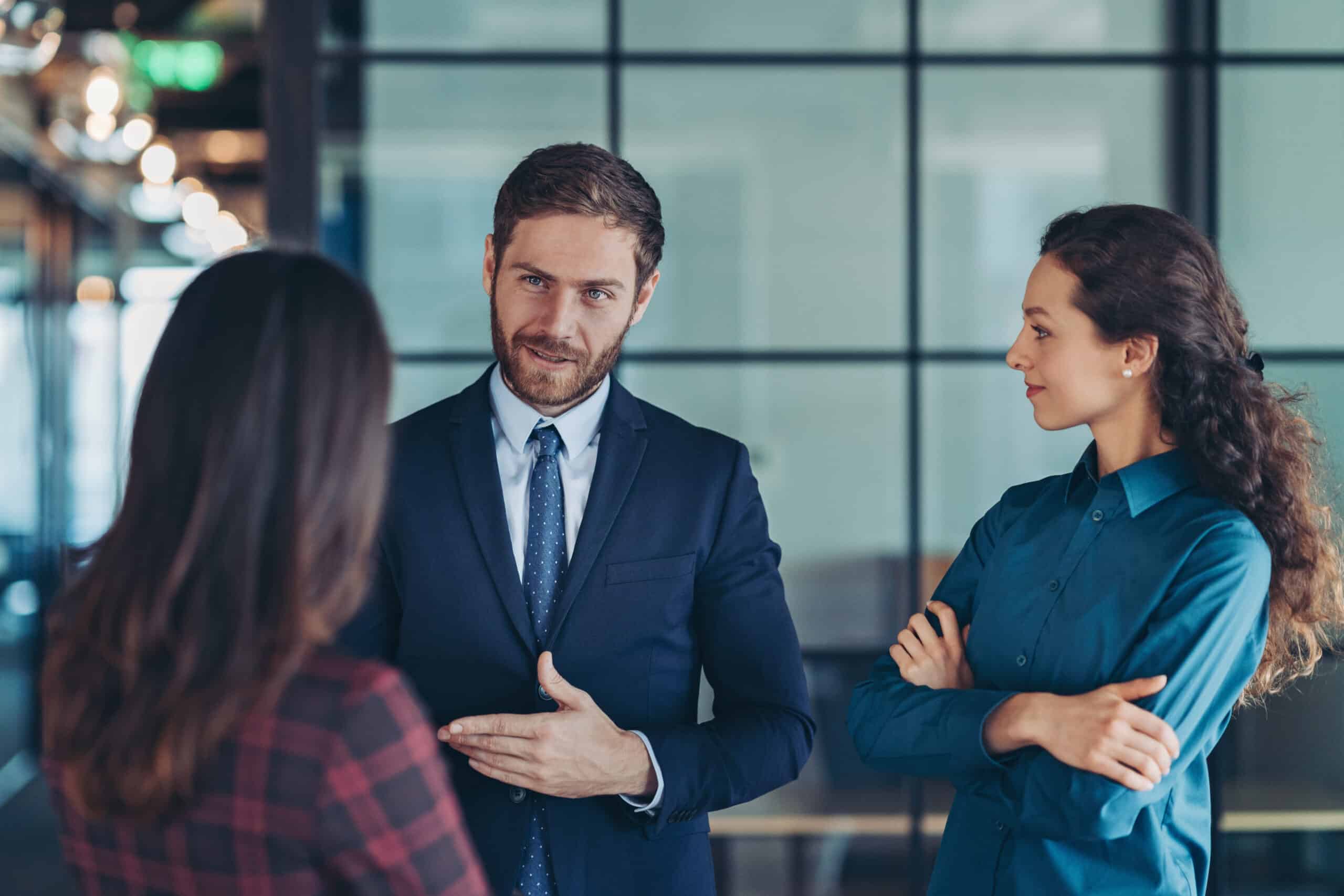 Three professionals discuss commercial real estate expense reduction in a modern glass-walled office.