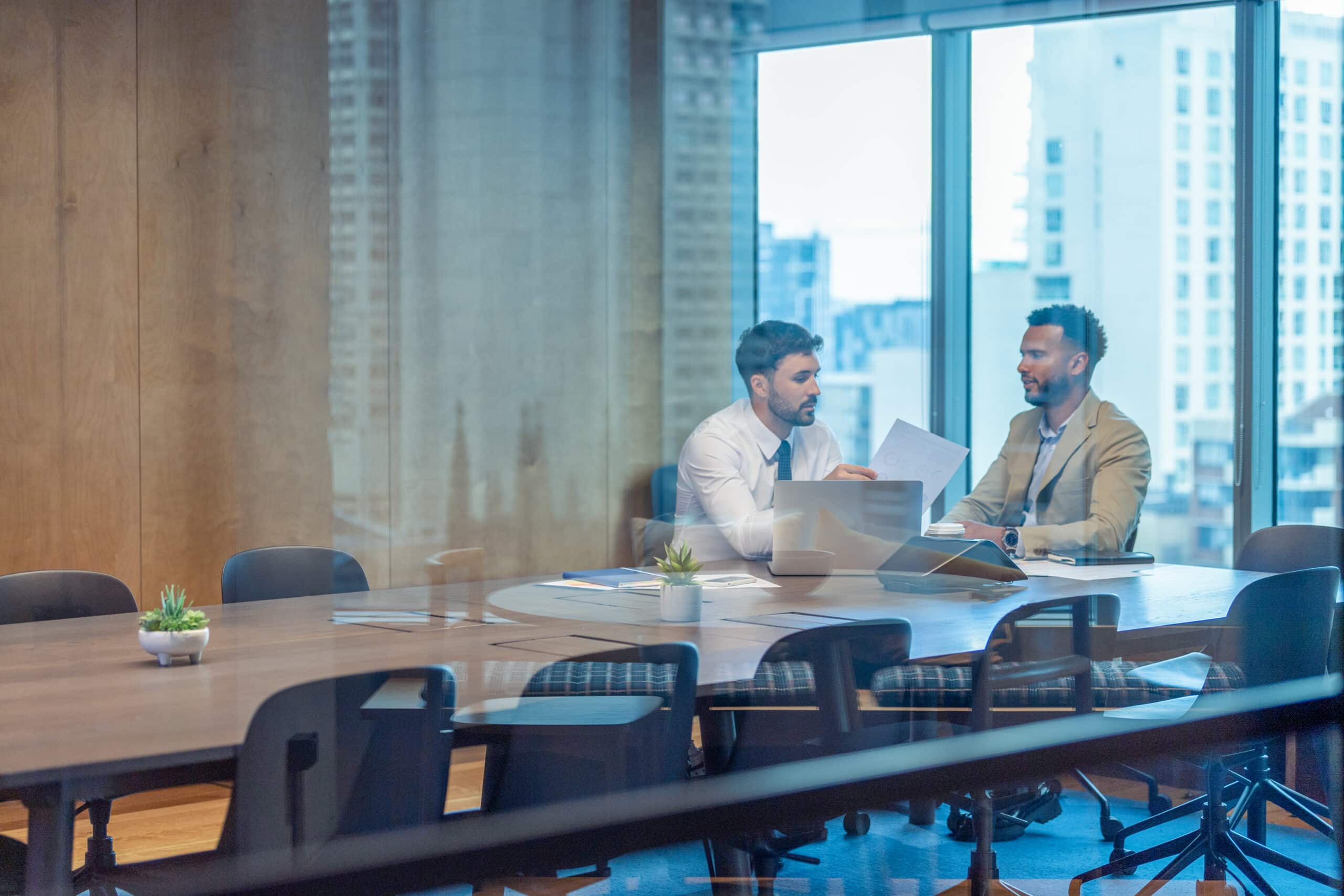 Two men in business attire discuss documents on commercial real estate operations consulting.