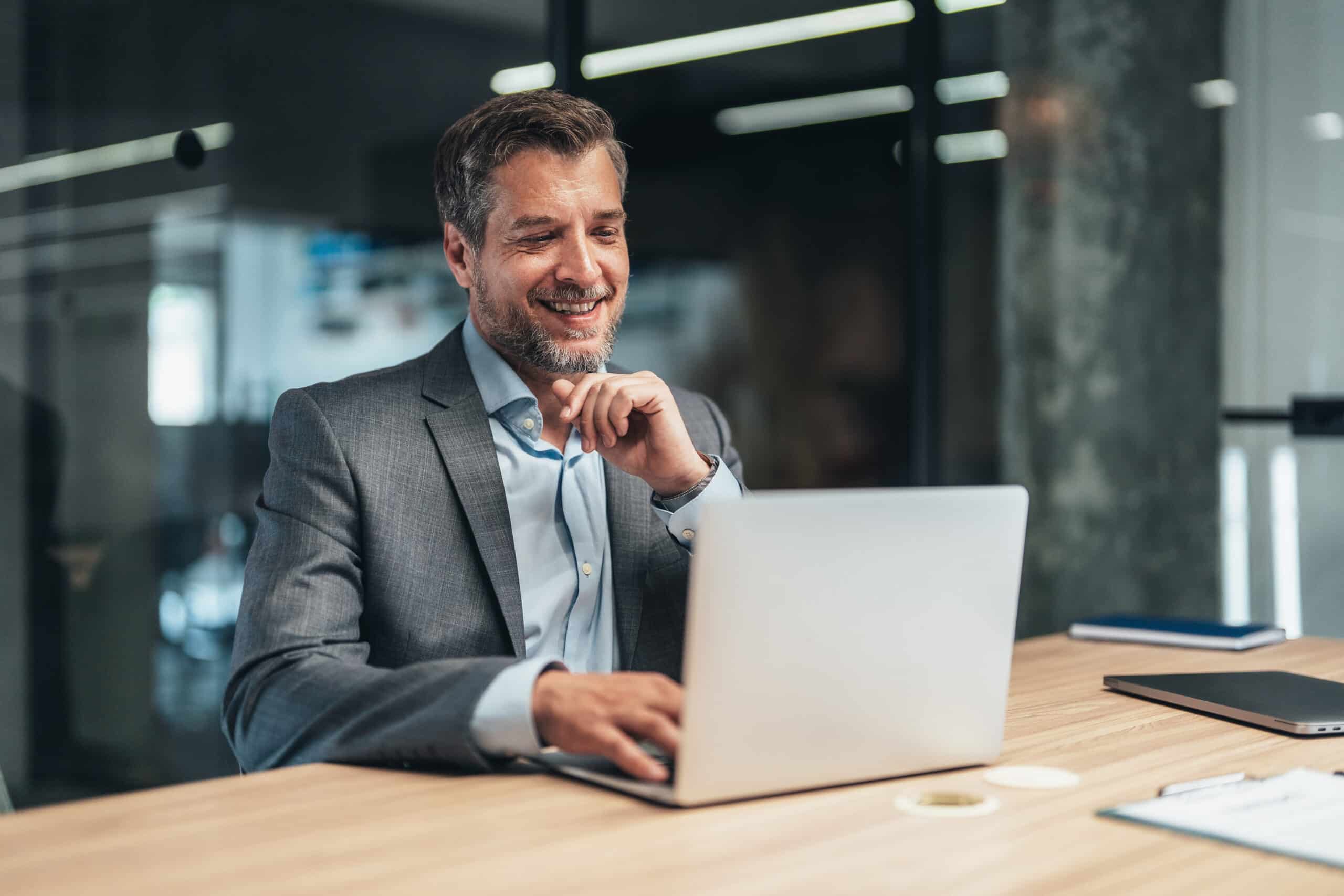 Smiling man in a suit works on a laptop, offering commercial real estate portfolio management.