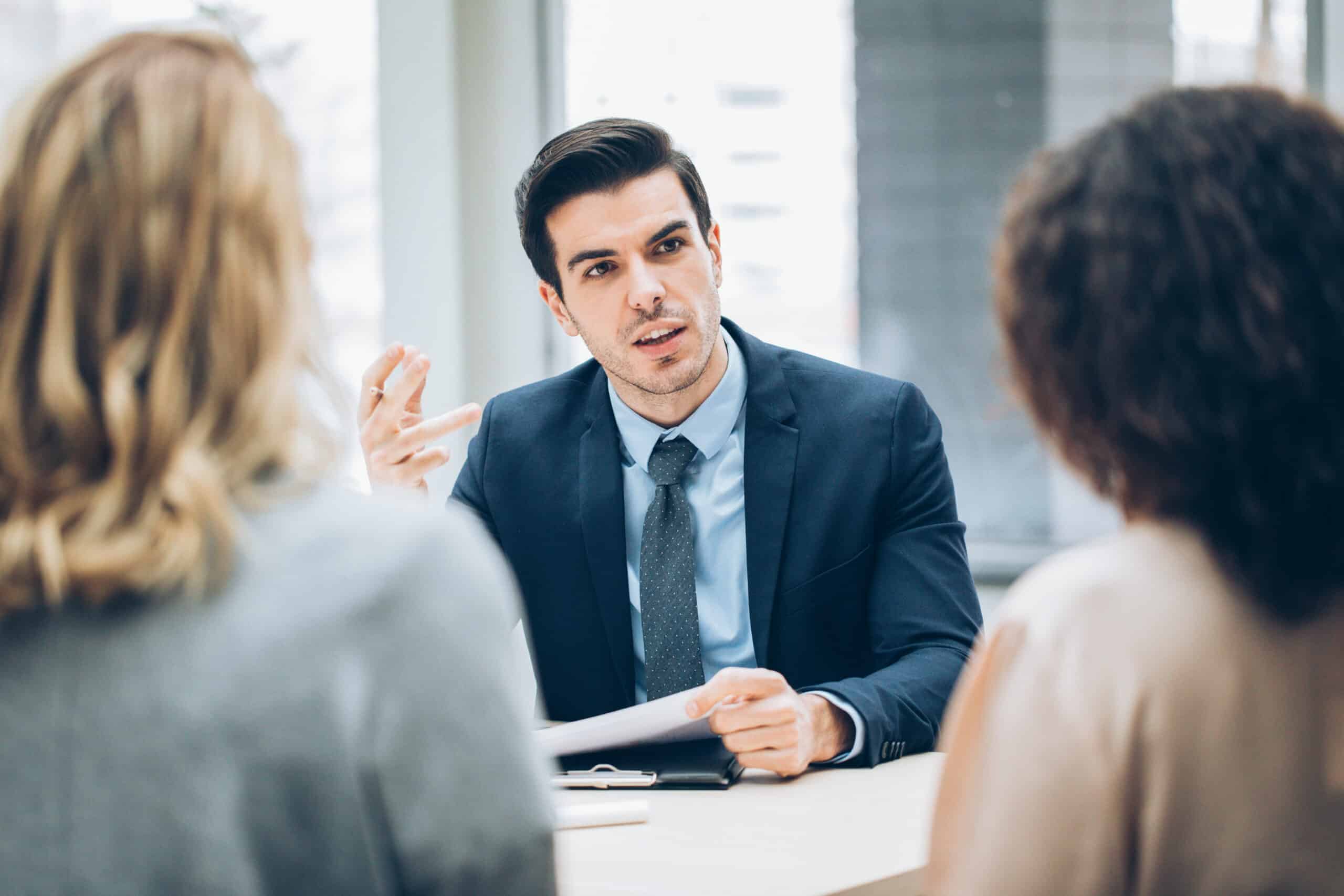 Man in suit consults with two women on commercial real estate portfolio management.